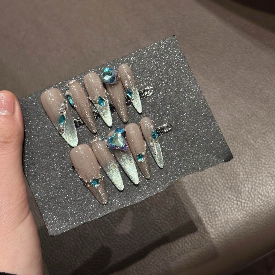 Embrace cosmic elegance with Celestial Frost Press-On Nails. These extra-long stiletto nails feature a stunning nude-to-silver gradient, accented with shimmering metallic details and radiant blue gemstones. The dazzling heart-shaped crystal centerpiece adds a touch of ethereal beauty, while delicate silver embellishments create a celestial, icy-glam aesthetic.