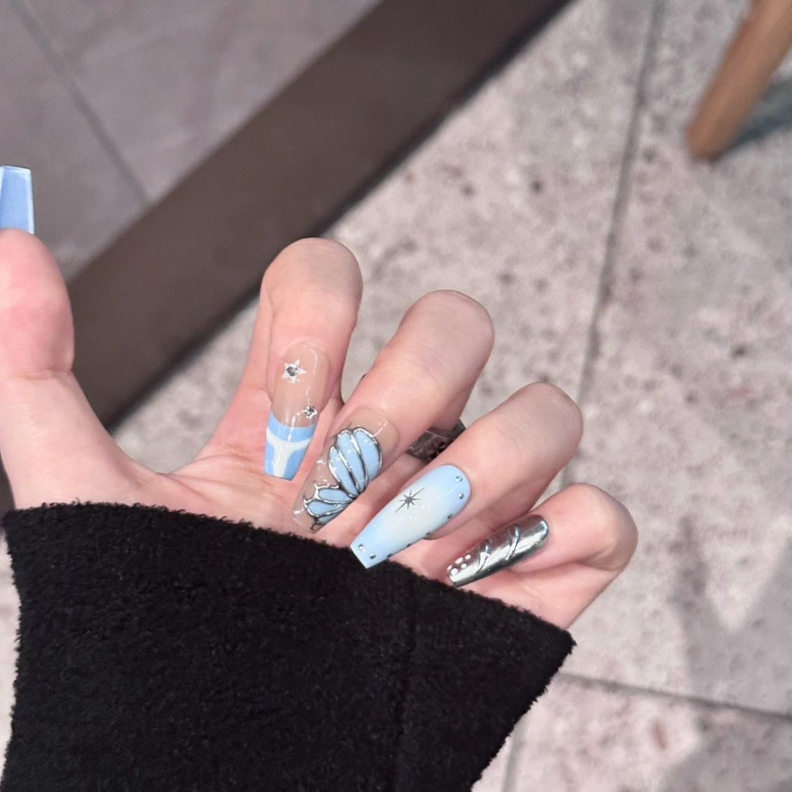 Celestial Tide Press-On Nails blend cosmic elegance with oceanic serenity, featuring a dreamy mix of soft blue, nude, and metallic silver. Delicate celestial stars, sculpted silver waves, and seashell-inspired details evoke the beauty of both the night sky and the deep sea. These nails create a sophisticated, ethereal look perfect for those who love a touch of magic in their style.
