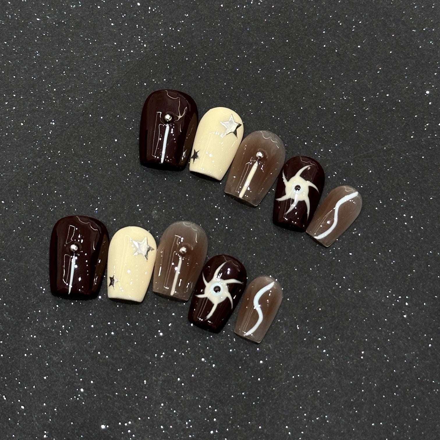 Explore the universe at your fingertips with Cosmic Dreams Press-On Nails, a celestial blend of deep burgundy, soft caramel gradients, and creamy ivory. This captivating set features cosmic star accents, abstract swirl designs, and subtle rhinestone embellishments, creating a mystical, galaxy-inspired look. The rich, earthy tones combined with bold star motifs evoke the magic of a starlit night sky, perfect for those who love a dreamy, ethereal aesthetic.