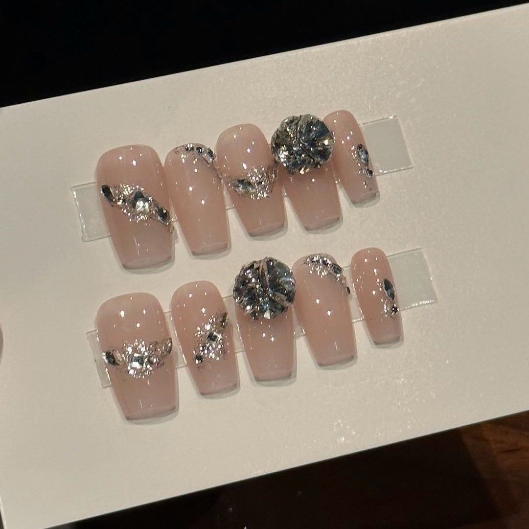 Step into luxurious elegance with Crystal Couture Press-On Nails, a glamorous blend of nude blush pink and dazzling silver gemstones. This sophisticated set features bold 3D crystal embellishments and delicate silver accents that sparkle with every movement, creating an opulent, high-fashion look. With a glossy finish and classic coffin shape, Crystal Couture brings a touch of red-carpet glamour to your fingertips.