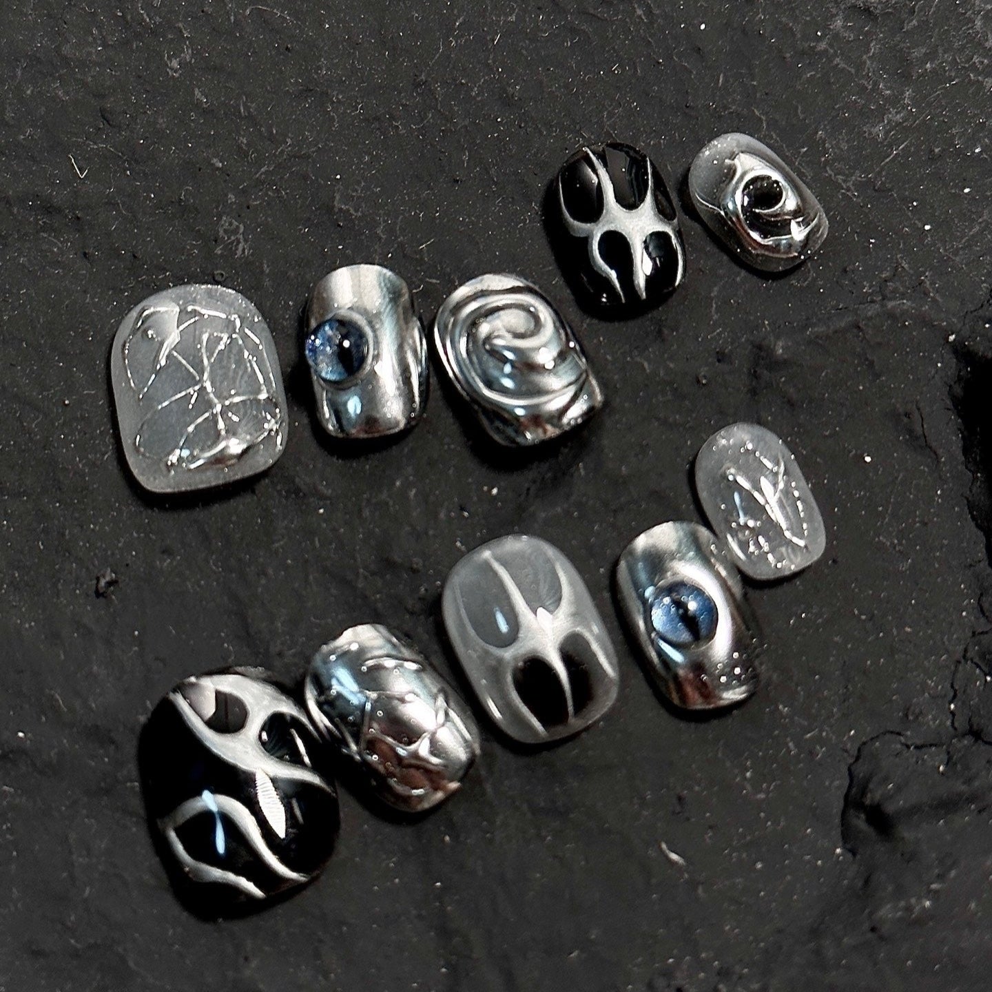 Step into the future with Cyber Gaze Press-On Nails. These short, round-shaped nails feature a striking silver and black color palette with intricate 3D sculpted designs. The bold, futuristic pattern is highlighted by two mesmerizing blue eyes that seem to peer through the metallic landscape, adding an edgy, otherworldly vibe.