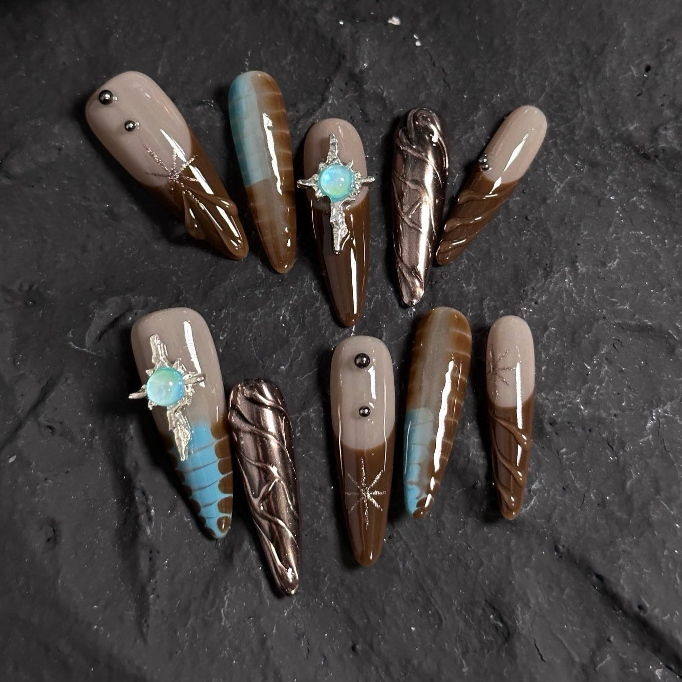 Embrace the mystique of the desert with Desert Dusk Press-On Nails, a stunning blend of earthy browns, sandy taupes, and turquoise accents. This set features intricate feather patterns, metallic bronze details, and opalescent gemstone embellishments, evoking the beauty of a sunlit desert oasis. The glossy finish and elongated stiletto shape add a touch of elegance and drama, perfect for those who love a boho-chic, nature-inspired aesthetic.