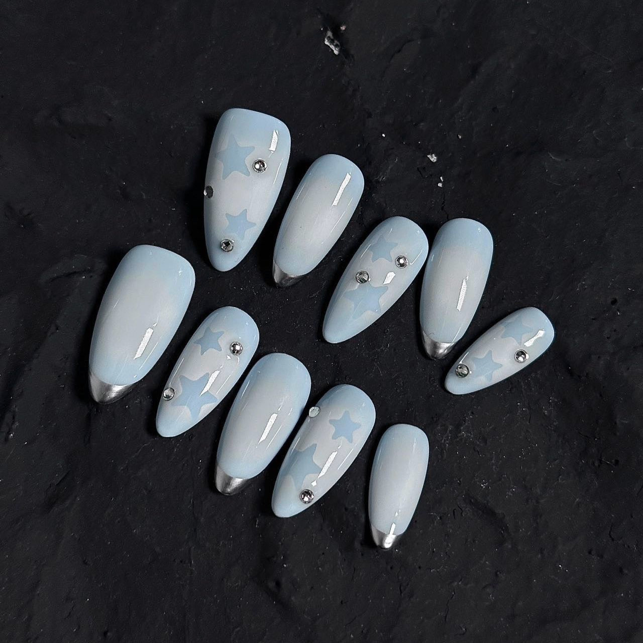 Float on a dreamy sky with Dreamy Skies Press-On Nails, a delicate blend of powder blue gradients, soft star motifs, and metallic silver tips. This whimsical set features a serene ombre effect, transitioning from light blue to pale white, reminiscent of a peaceful, cloudy sky. Adorned with subtle silver accents and ethereal star patterns, Dreamy Skies brings a touch of magic and serenity to your fingertips.