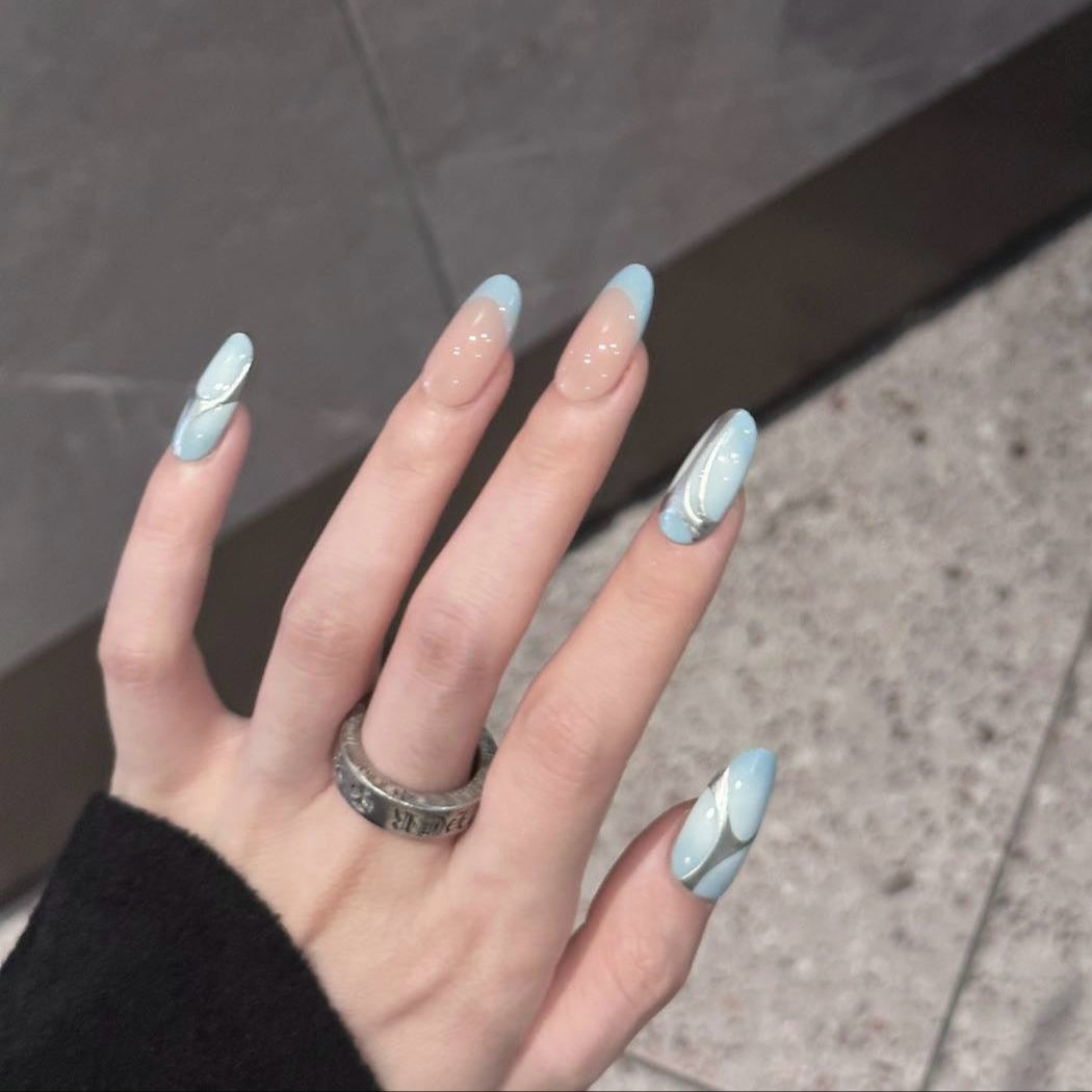 Ethereal Flow Press-On Nails capture the harmony between earth and sky, blending soft pastel blue with a warm nude base for a natural yet artistic appeal. Featuring sleek, silver fluid accents that mimic the graceful movement of water and air, this set embodies elegance with a modern twist.