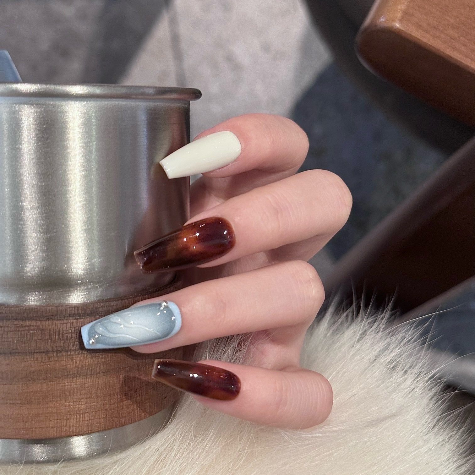 Embrace the contrast of cool elegance and warm intensity with Frost & Ember Press-On Nails. This striking set features a dual-tone design, blending icy blue cat-eye shimmer, creamy ivory, and deep amber brown for a bold yet sophisticated look. The sleek coffin shape adds a modern, elongated finish, while subtle rhinestone accents bring a touch of refined luxury.