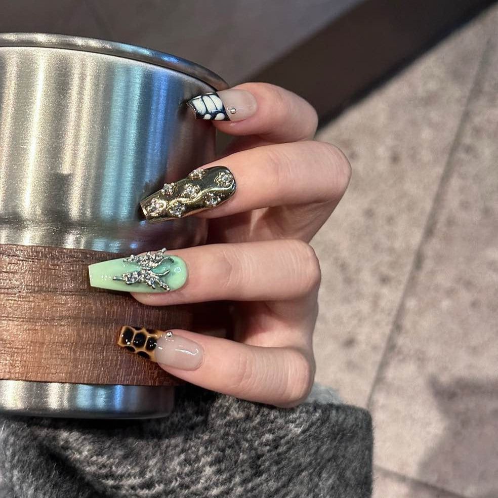 Channel bold luxury with Gilded Serpent Press-On Nails, an exotic fusion of rich jewel tones, metallic textures, and intricate embellishments. This opulent set features deep burgundy, jade green, and soft taupe hues, accentuated with snakeskin-inspired patterns, reflective gold chrome, and striking 3D silver charms. The blend of textures—smooth glossy finishes, sculpted reptilian details, and shimmering crystal accents—creates an edgy yet elegant masterpiece for your fingertips.