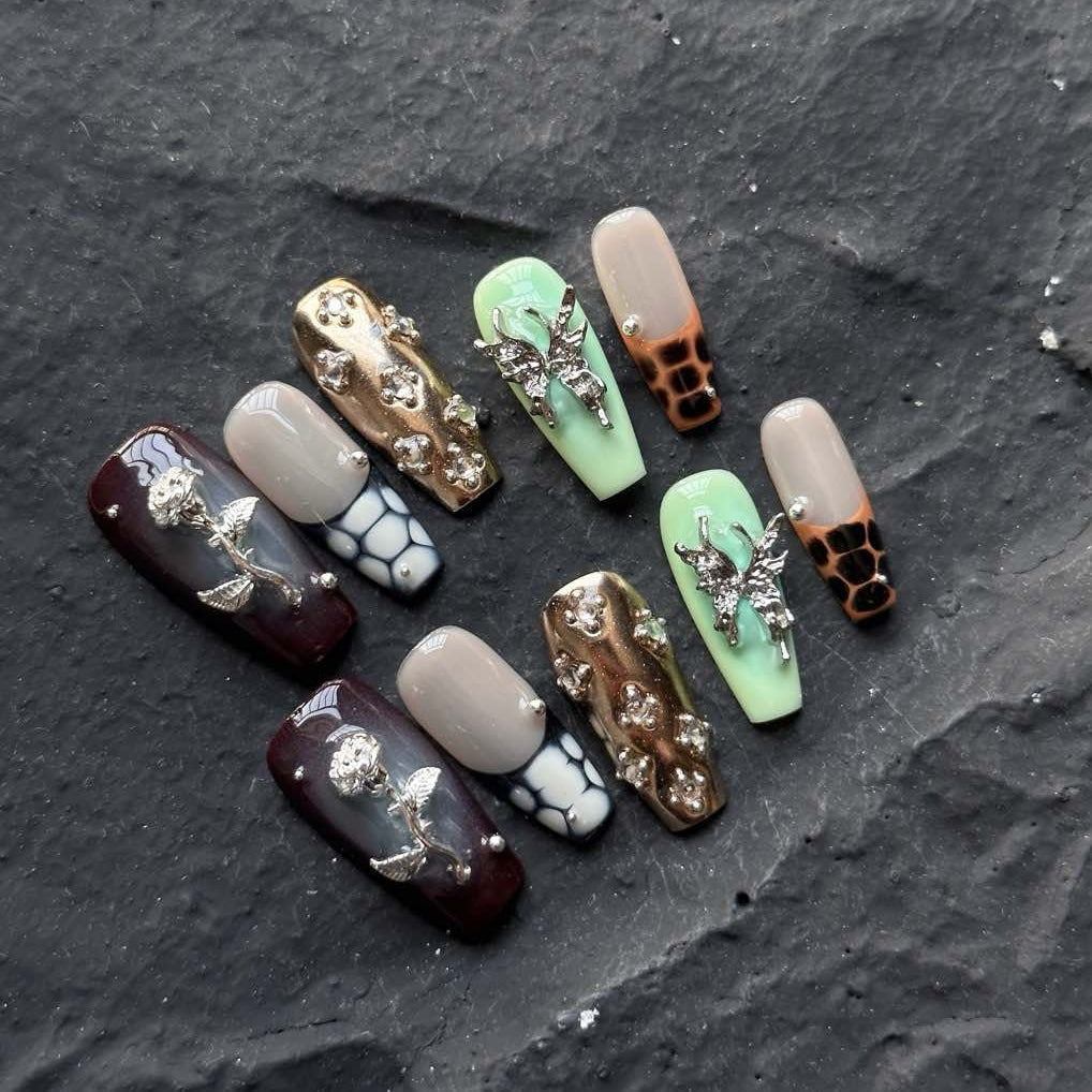 Channel bold luxury with Gilded Serpent Press-On Nails, an exotic fusion of rich jewel tones, metallic textures, and intricate embellishments. This opulent set features deep burgundy, jade green, and soft taupe hues, accentuated with snakeskin-inspired patterns, reflective gold chrome, and striking 3D silver charms. The blend of textures—smooth glossy finishes, sculpted reptilian details, and shimmering crystal accents—creates an edgy yet elegant masterpiece for your fingertips.