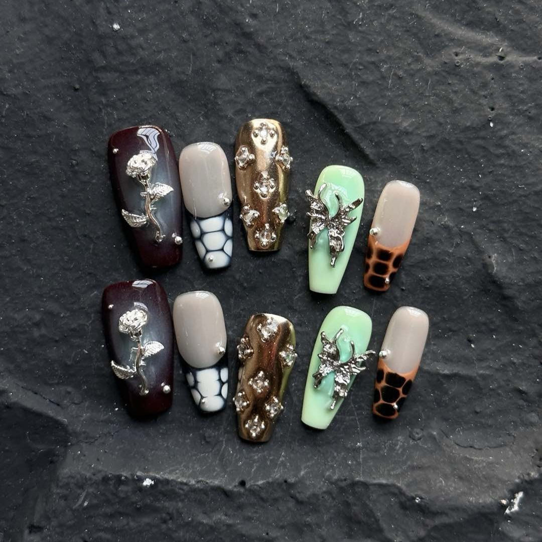 Channel bold luxury with Gilded Serpent Press-On Nails, an exotic fusion of rich jewel tones, metallic textures, and intricate embellishments. This opulent set features deep burgundy, jade green, and soft taupe hues, accentuated with snakeskin-inspired patterns, reflective gold chrome, and striking 3D silver charms. The blend of textures—smooth glossy finishes, sculpted reptilian details, and shimmering crystal accents—creates an edgy yet elegant masterpiece for your fingertips.
