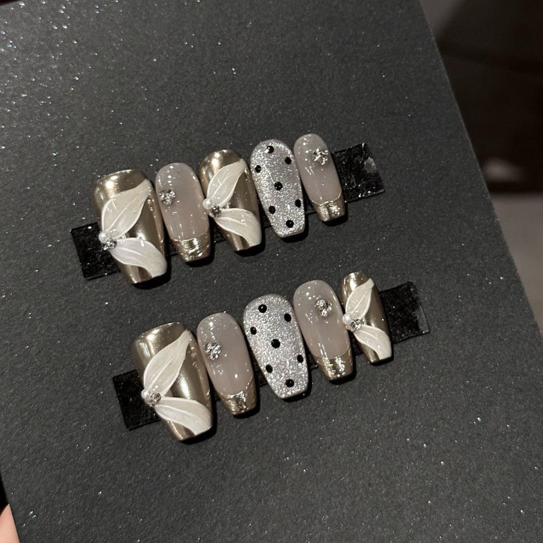 Glamour Noir Press-On Nails bring a sophisticated edge to your look with a chic palette of metallic silver, smoky grey, and bold black polka dots. Designed with elegant 3D ribbon accents and sparkling rhinestones, these nails offer a timeless yet modern flair perfect for evenings out or adding a touch of luxury to any outfit.
