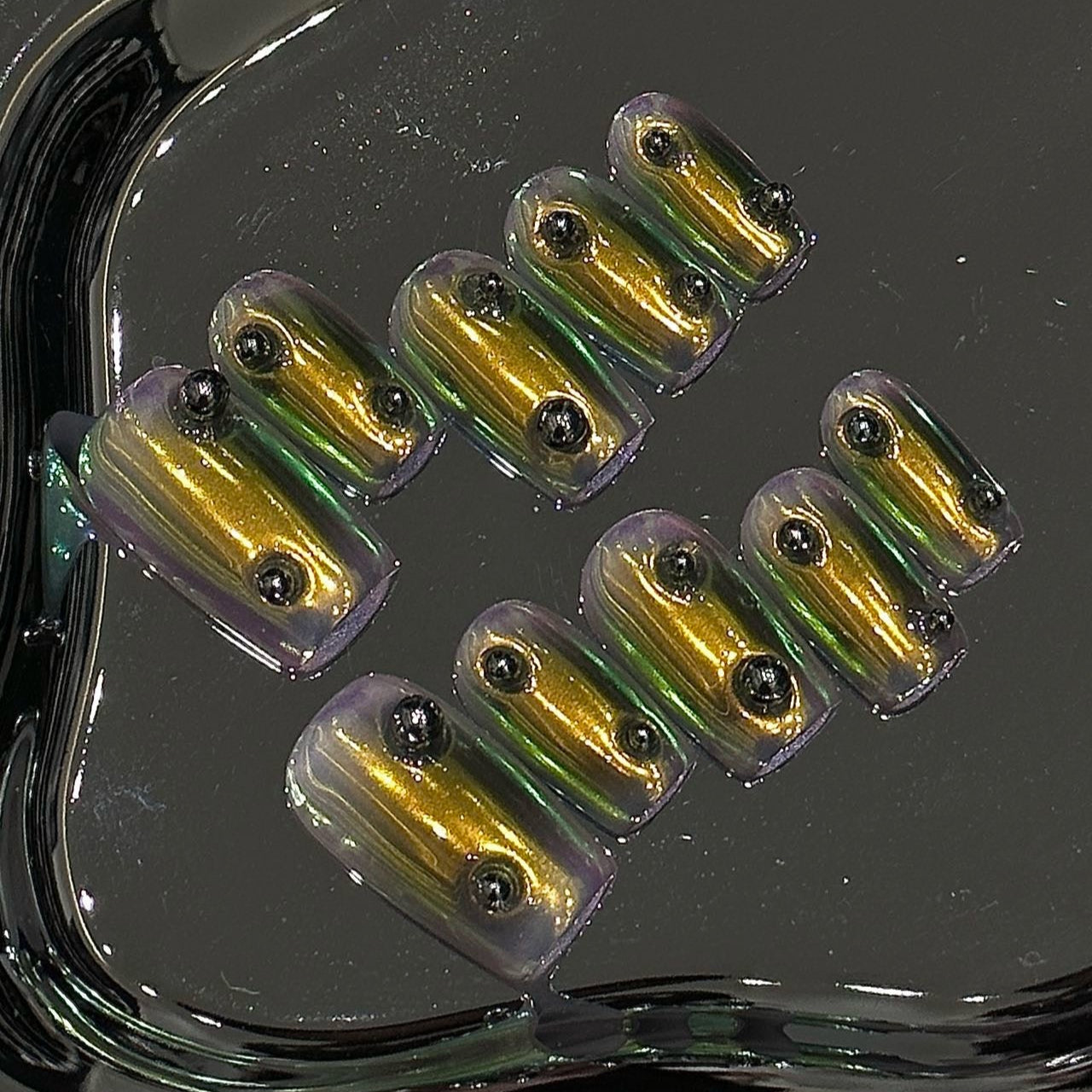 Unleash futuristic elegance with Golden Beetle Press-On Nails, a mesmerizing blend of metallic gold and iridescent green chrome. This striking set features a bold, reflective finish that shifts between shades of gold and emerald, inspired by the mesmerizing exoskeleton of a jewel beetle. Adorned with sleek black studs for an edgy, industrial touch, Golden Beetle brings a bold, avant-garde statement to your fingertips.
