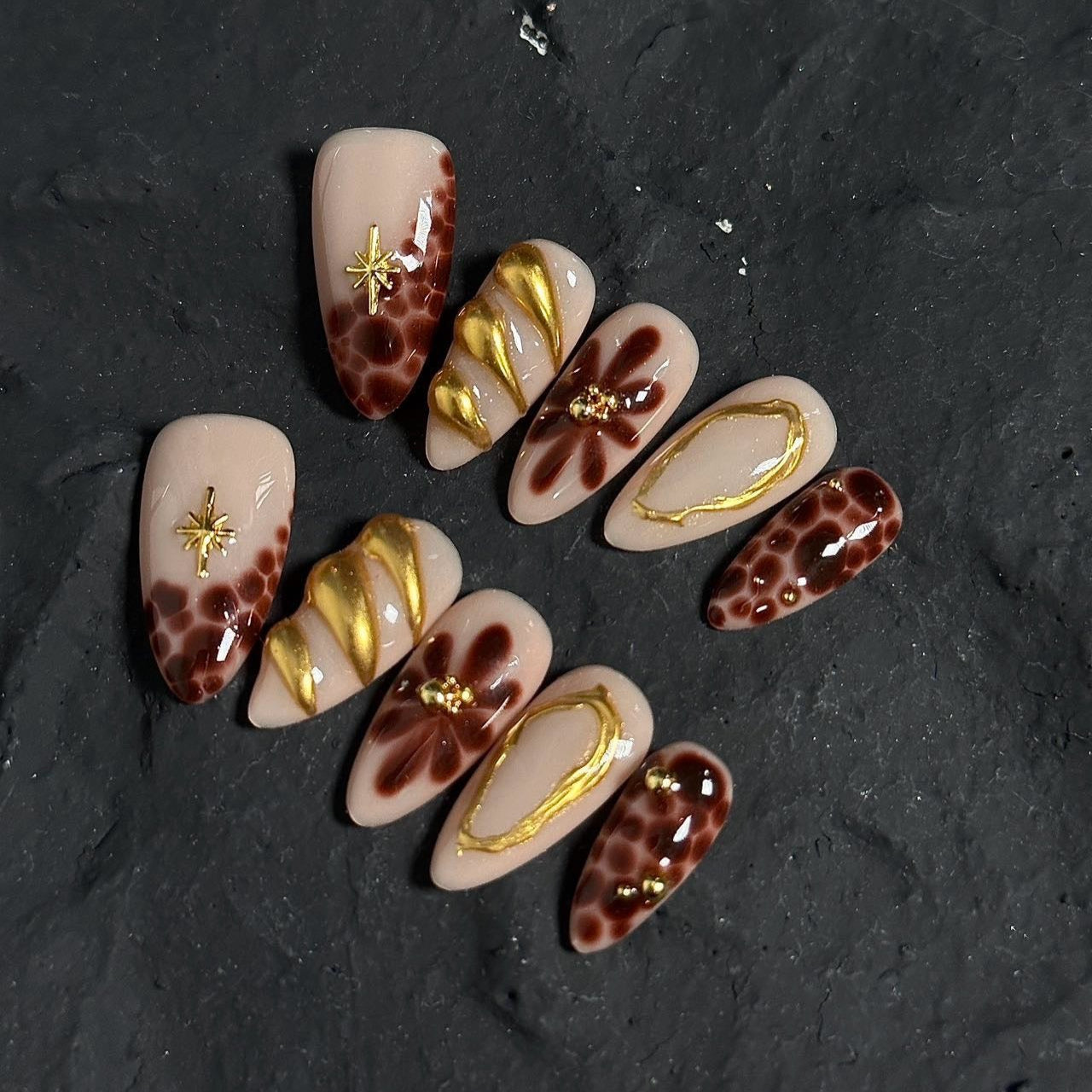 Unleash your wild side with Golden Leopard Press-On Nails, a fierce blend of rich chocolate leopard print, nude-beige base, and luxurious gold accents. This bold set features intricate animal patterns, sculpted gold embellishments, and shimmering star motifs, creating an exotic and glamorous look. The sleek almond shape adds a chic, elongated finish, perfect for those who love a luxurious, fashion-forward aesthetic.