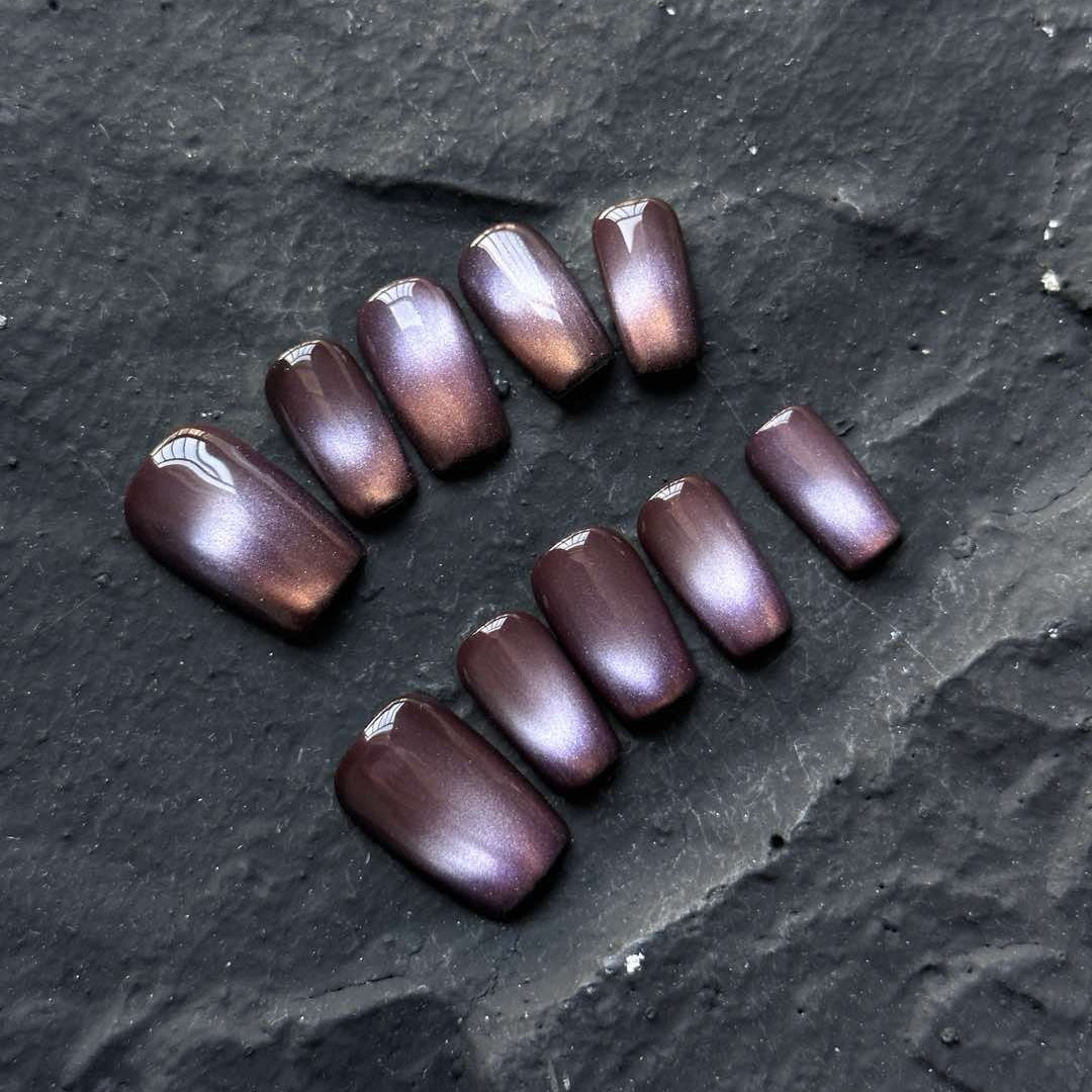 Ignite your look with Midnight Ember Press-On Nails, a mesmerizing blend of deep plum and fiery bronze hues. This set features a rich, cat-eye shimmer effect that shifts with the light, creating an enchanting glow reminiscent of glowing embers against a midnight sky. The smooth, high-gloss finish enhances the depth and intensity of the colors, giving your nails an effortlessly luxurious touch.