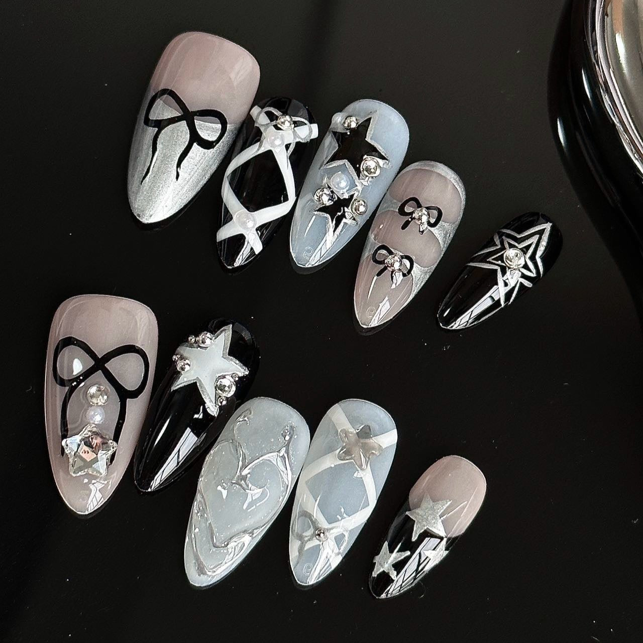 Midnight Galaxy Press-On Nails capture the mystique of the cosmos with a bold blend of black, silver, and soft grey shades. Featuring intricate star motifs, geometric patterns, and 3D bow embellishments, these nails offer a look that is both elegant and futuristic.