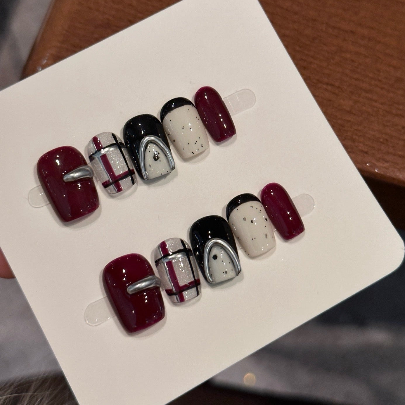 Step into bold sophistication with Midnight Plaid Press-On Nails, a chic blend of deep burgundy, glossy black, and creamy ivory tones enhanced with metallic silver accents. This set features a modern plaid pattern, glossy solids, and edgy chrome details, creating a contemporary yet timeless look. With a playful mix of patterns and minimalist speckles, Midnight Plaid is the perfect fusion of classic elegance and urban flair.
