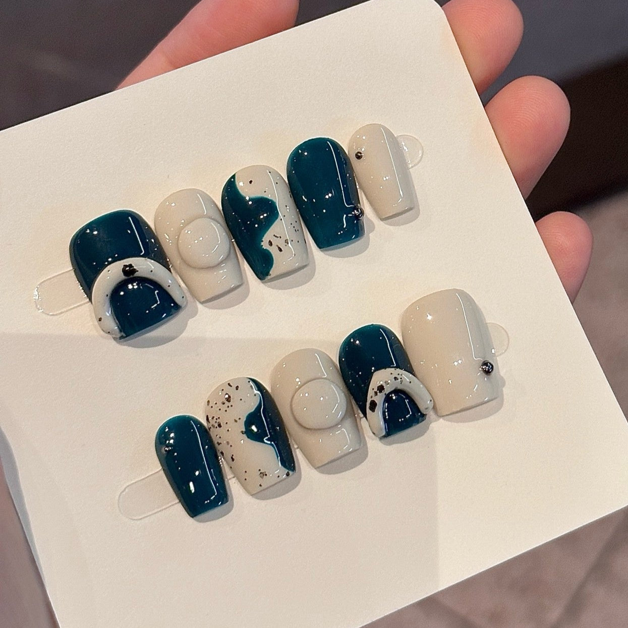 Step into contemporary style with Modern Abstract Press-On Nails, a chic blend of deep teal and creamy ivory enhanced with minimalist geometric patterns and artistic splatter effects. This sophisticated set features bold, abstract shapes and a glossy finish that creates a sleek, modern look. With a structured short square shape, Modern Abstract brings an avant-garde, artistic vibe to your fingertips.