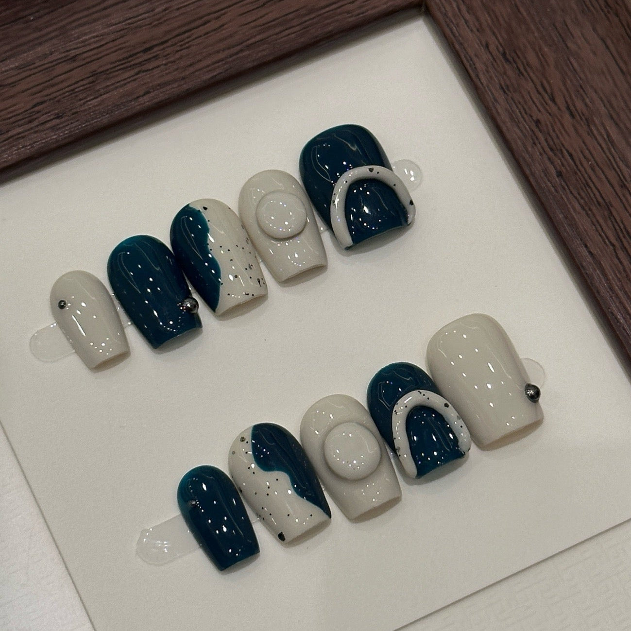 Step into contemporary style with Modern Abstract Press-On Nails, a chic blend of deep teal and creamy ivory enhanced with minimalist geometric patterns and artistic splatter effects. This sophisticated set features bold, abstract shapes and a glossy finish that creates a sleek, modern look. With a structured short square shape, Modern Abstract brings an avant-garde, artistic vibe to your fingertips.