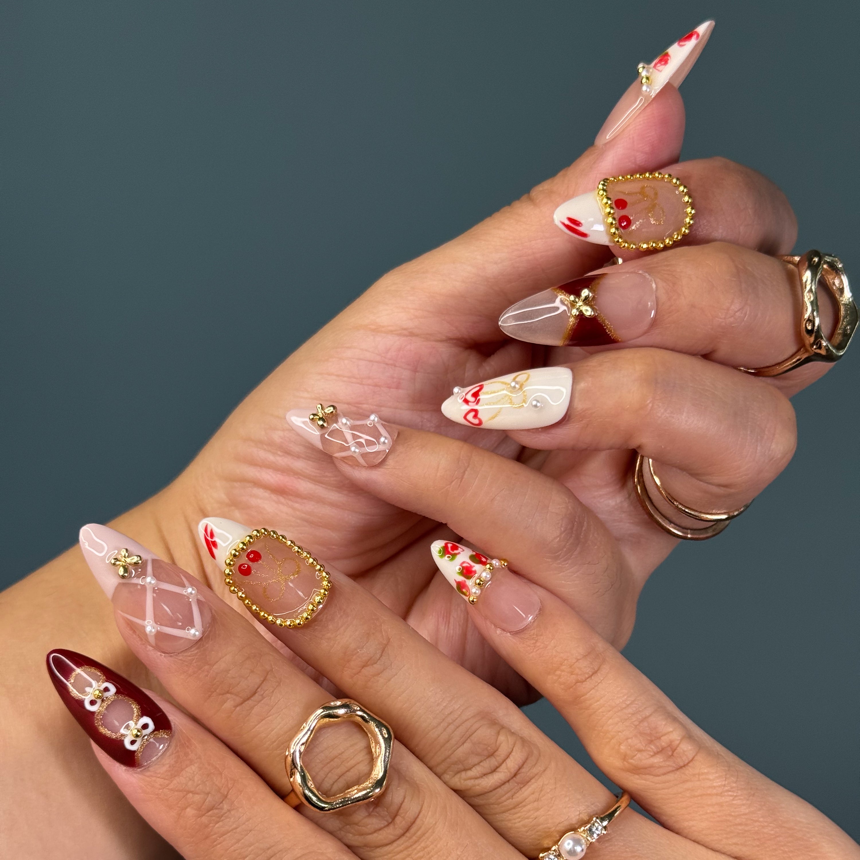  Classic Color Story: Deep wine reds, nude taupes, and ivory creams for a timeless, romantic vibe.
• 3D Gold Beading: Framed accents and metallic details give the look of ornate vintage jewelry.
• Cherry & Heart Motifs: Hand-painted fruits and dangling hearts add a playful, romantic twist.
• Bow and Lattice Designs: Intricate patterns evoke lace, corsetry, and old-world luxury.
• Almond Shape: A refined, feminine silhouette that elevates the opulent designs.