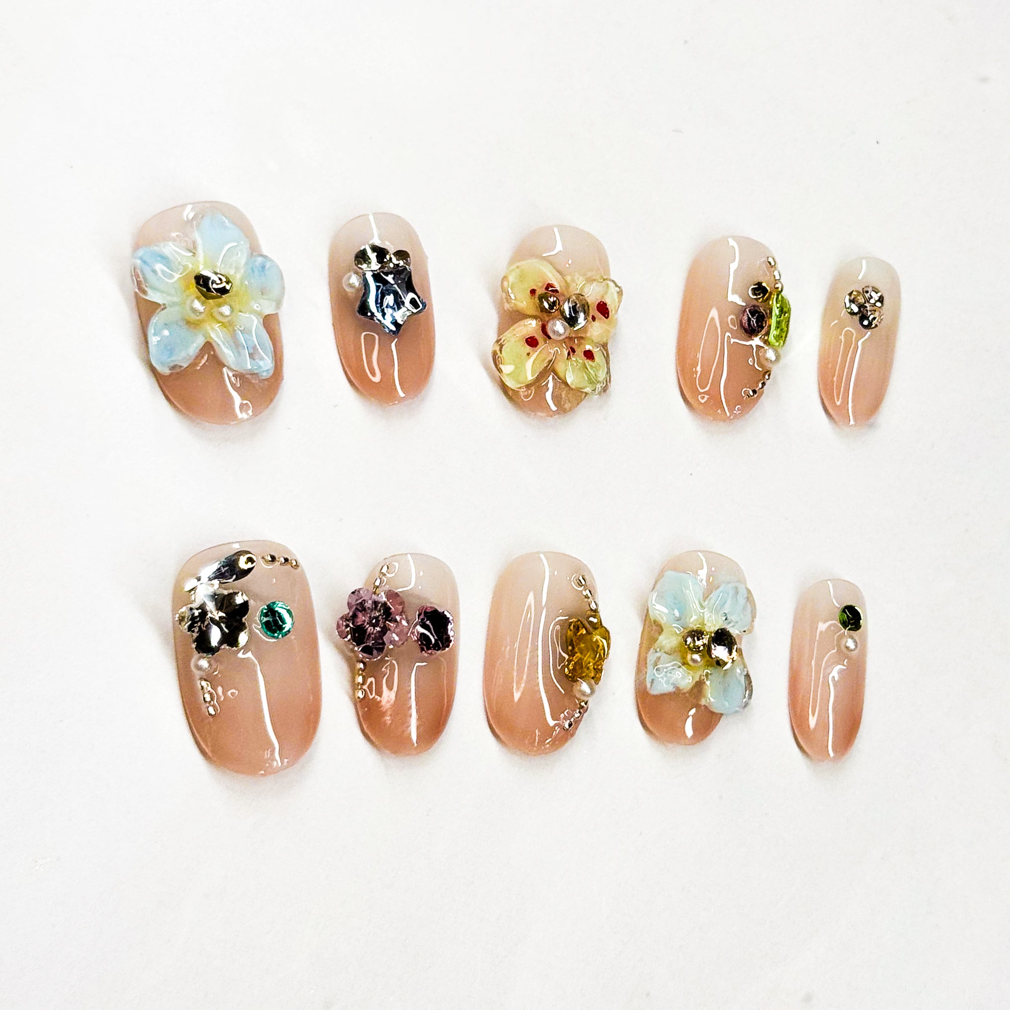 3D Florals: Handcrafted flowers in pastel blue, sunshine yellow, and soft metallic accents.
• Sparkling Crystals: Jewel embellishments in emerald, amethyst, and citrine tones.
• Nude Base: Soft, glossy nude backdrop for a timeless, chic foundation.
• Short Square Shape: Practical yet elegant, perfect for everyday wear.
• Handcrafted Luxury: Each piece is unique with artisanal detailing.