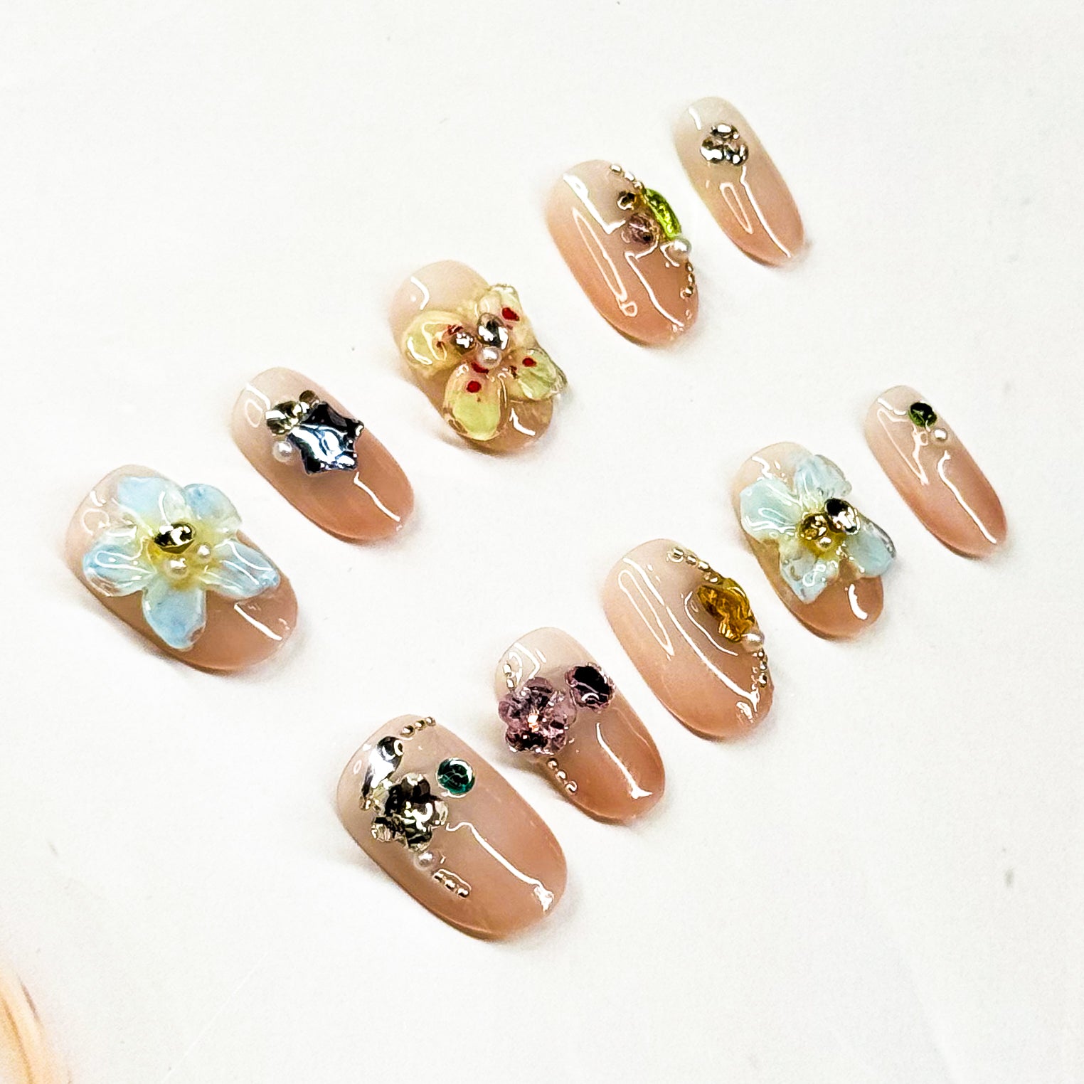 3D Florals: Handcrafted flowers in pastel blue, sunshine yellow, and soft metallic accents.
• Sparkling Crystals: Jewel embellishments in emerald, amethyst, and citrine tones.
• Nude Base: Soft, glossy nude backdrop for a timeless, chic foundation.
• Short Square Shape: Practical yet elegant, perfect for everyday wear.
• Handcrafted Luxury: Each piece is unique with artisanal detailing.