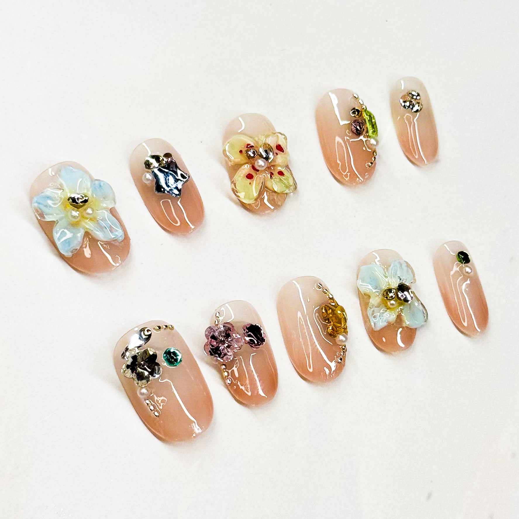 3D Florals: Handcrafted flowers in pastel blue, sunshine yellow, and soft metallic accents.
• Sparkling Crystals: Jewel embellishments in emerald, amethyst, and citrine tones.
• Nude Base: Soft, glossy nude backdrop for a timeless, chic foundation.
• Short Square Shape: Practical yet elegant, perfect for everyday wear.
• Handcrafted Luxury: Each piece is unique with artisanal detailing.