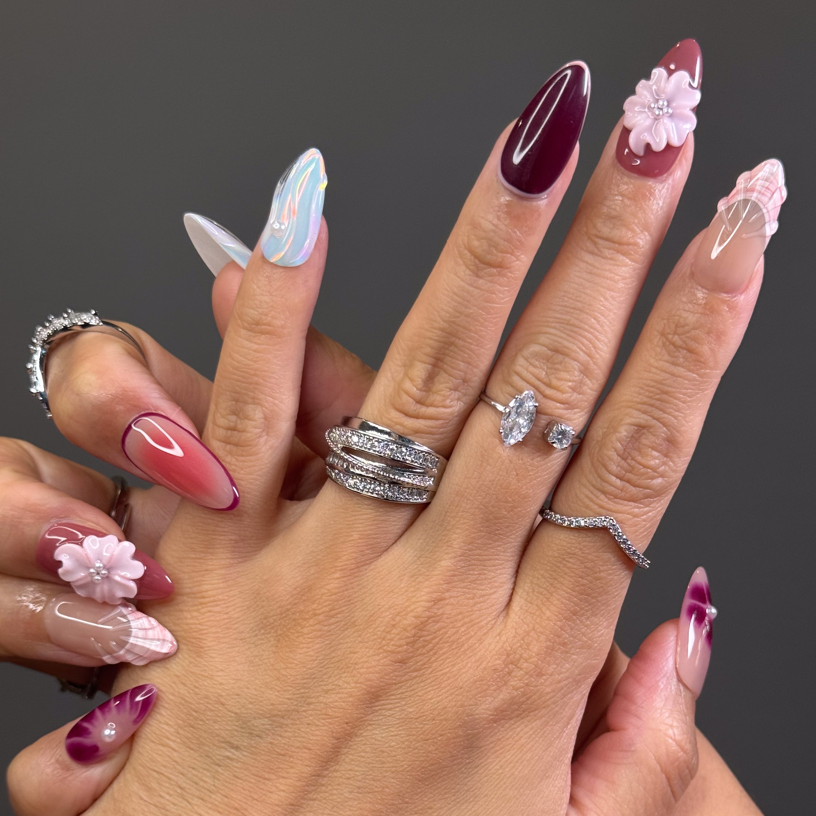 Rosy, Plum & Aqua Palette: A moody yet sweet mix of mauve, burgundy, shell beige, and ethereal pastel teal.
• 3D Blossoms & Shells: Hand-sculpted flowers and seashell ridges bring sculptural beauty and texture.
• Iridescent Swirls: Pastel wave patterns with a glowing pearl finish mimic soft ocean tides.
• Elegant Accents: Pearl beads and gradient effects add depth and femininity to each nail.
• Almond Shape: A gentle, elongated silhouette that enhances both softness and sophistication.