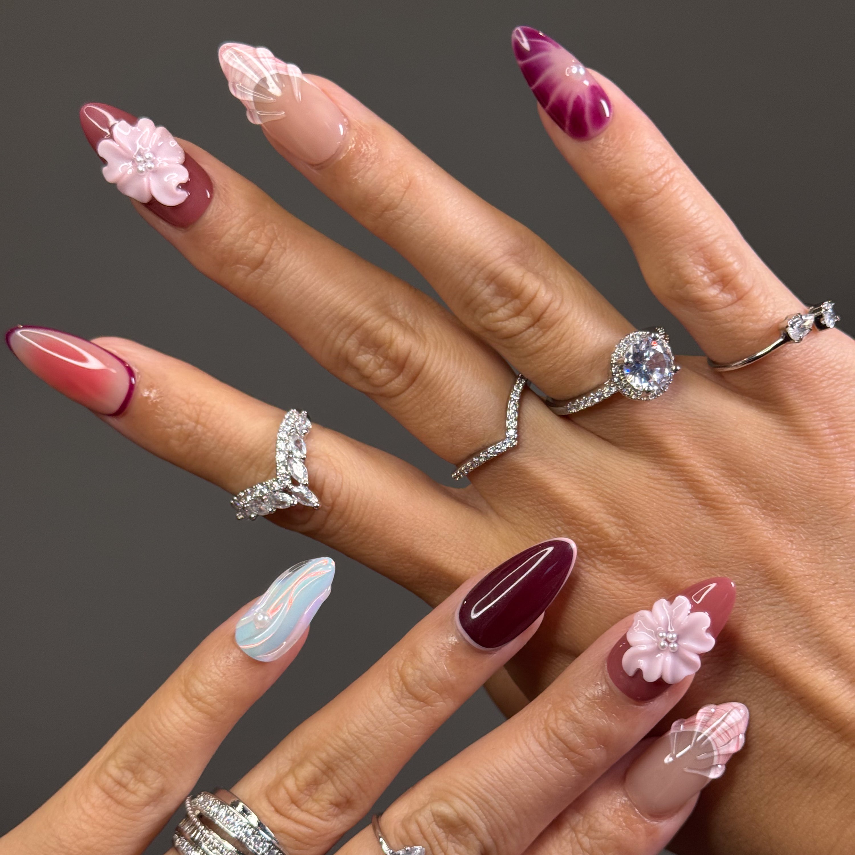 Rosy, Plum & Aqua Palette: A moody yet sweet mix of mauve, burgundy, shell beige, and ethereal pastel teal.
• 3D Blossoms & Shells: Hand-sculpted flowers and seashell ridges bring sculptural beauty and texture.
• Iridescent Swirls: Pastel wave patterns with a glowing pearl finish mimic soft ocean tides.
• Elegant Accents: Pearl beads and gradient effects add depth and femininity to each nail.
• Almond Shape: A gentle, elongated silhouette that enhances both softness and sophistication.