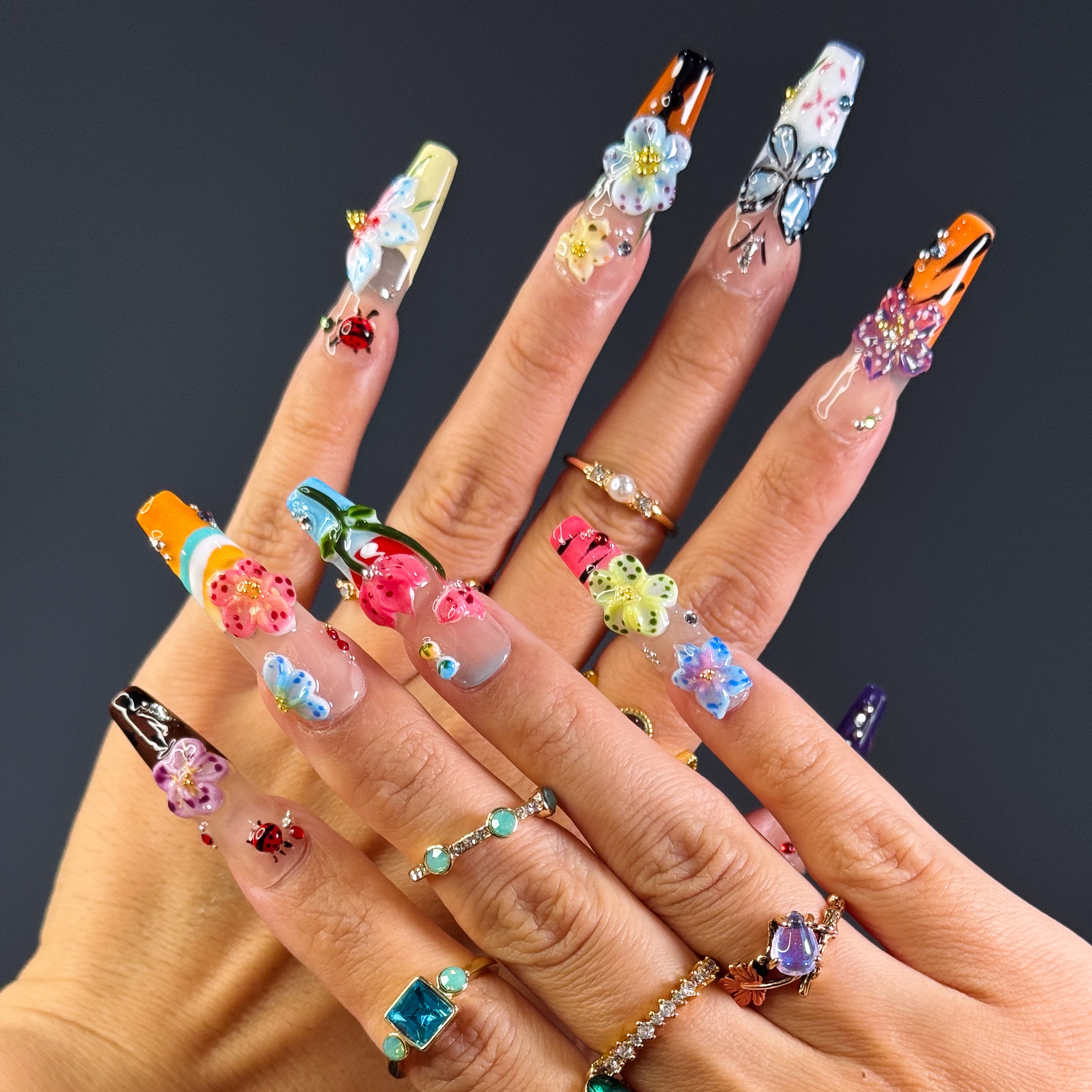 Vibrant Floral Palette: Hot pinks, teals, purples, yellows, and more—each nail like a wildflower in full bloom.
• 3D Garden Details: Sculpted butterflies, blossoms, and ladybugs bring a whimsical, storybook feel.
• Matte-to-Gloss Contrast: Smoky matte bases meet ultra-glossy, raised designs for textural drama.
• Nature-Inspired Artistry: Hand-painted stems, leaves, and wing details create a wearable garden on your fingertips.
• Long Coffin Shape: A sleek, squared-off silhouette perfect for showcasing