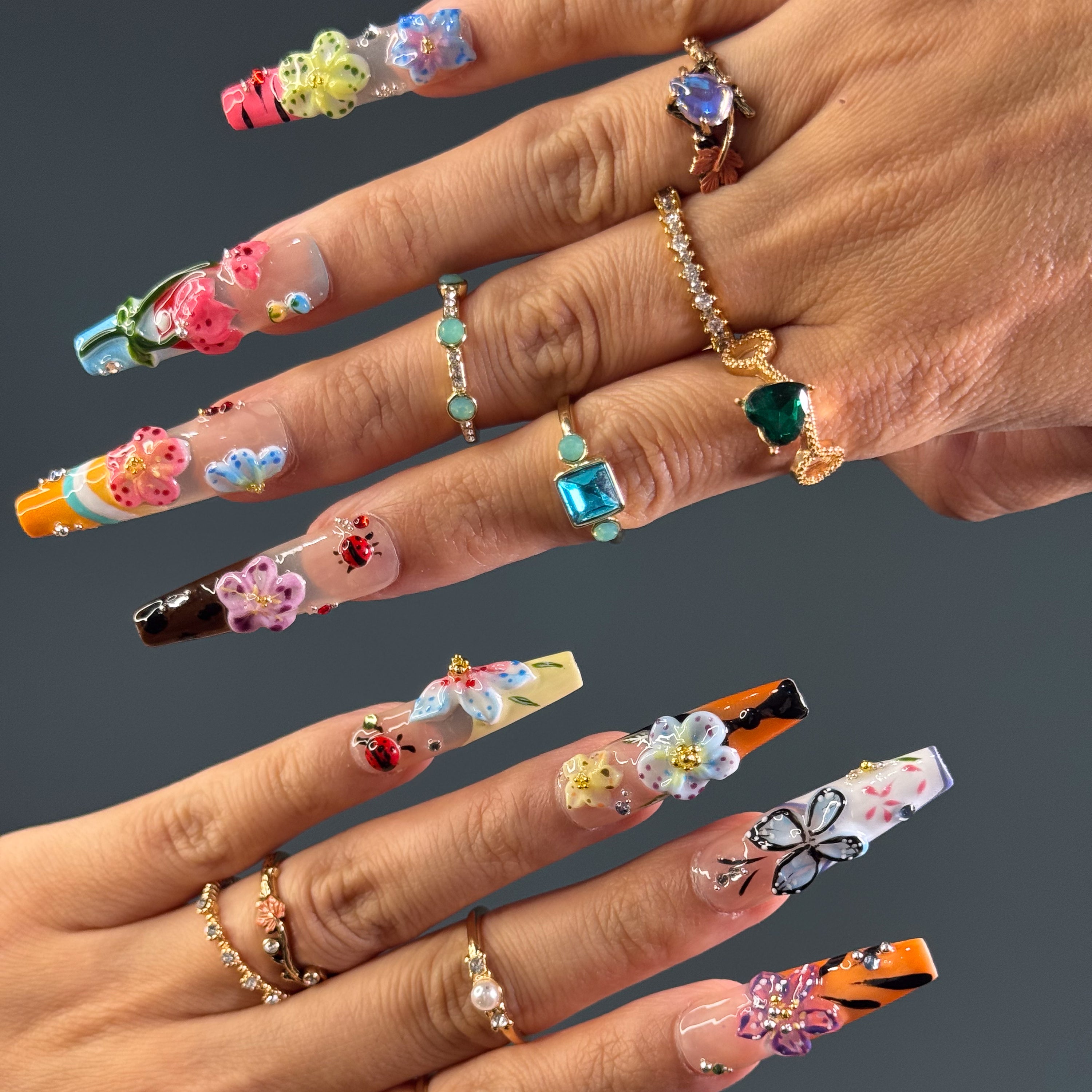 Vibrant Floral Palette: Hot pinks, teals, purples, yellows, and more—each nail like a wildflower in full bloom.
• 3D Garden Details: Sculpted butterflies, blossoms, and ladybugs bring a whimsical, storybook feel.
• Matte-to-Gloss Contrast: Smoky matte bases meet ultra-glossy, raised designs for textural drama.
• Nature-Inspired Artistry: Hand-painted stems, leaves, and wing details create a wearable garden on your fingertips.
• Long Coffin Shape: A sleek, squared-off silhouette perfect for showcasing