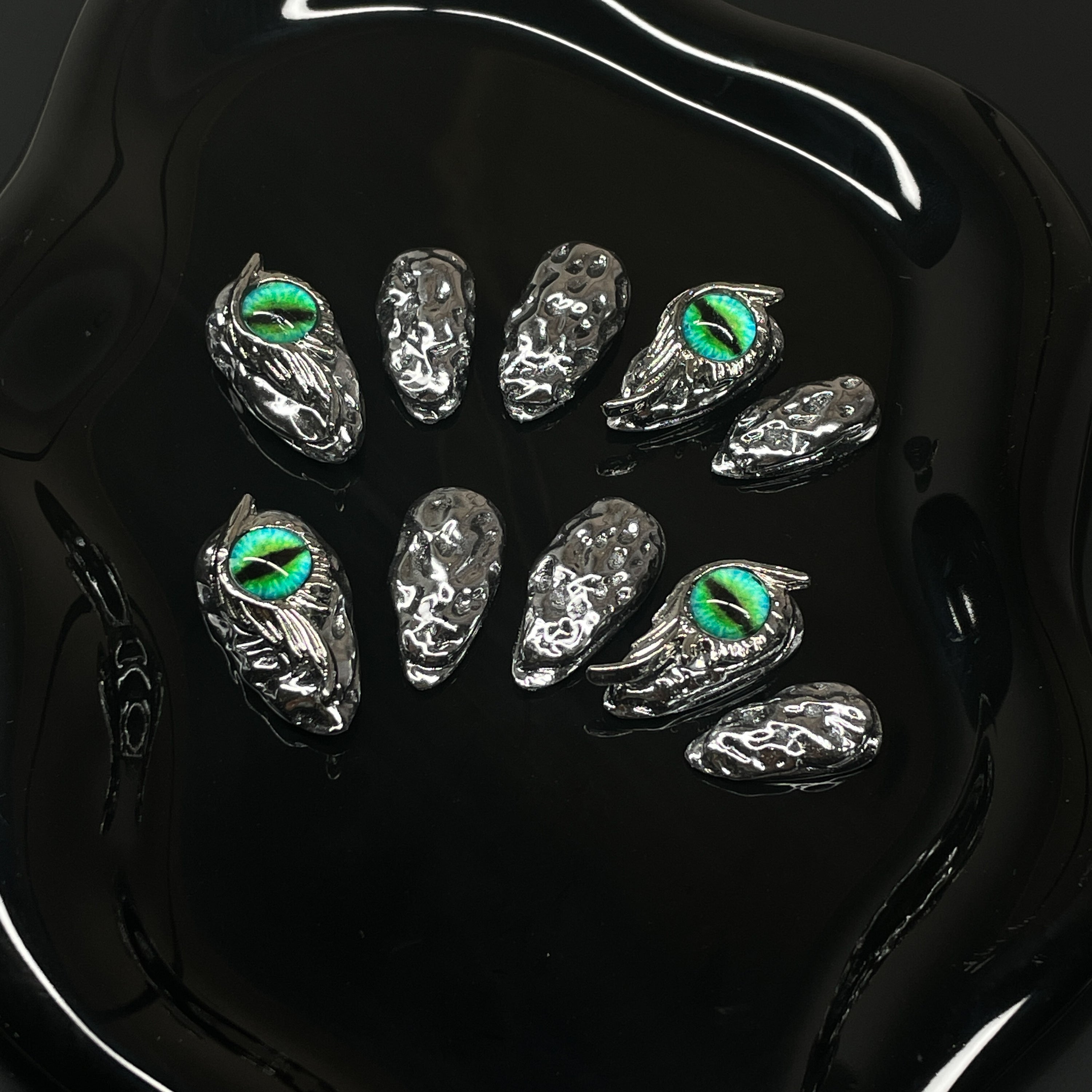 Chrome Scale Texture: Irregular molten metal surface mimics dragon hide with a futuristic edge.
• Striking Green Eyes: Hand-placed dragon eye orbs add hypnotic intensity and a fierce focal point.
• 3D Sculpted Armor: Metallic claws and raised textures evoke a battle-ready fantasy aesthetic.
• High-Shine Finish: Ultra-reflective silver coating for a sleek, high-impact look.
• Almond Shape: Balanced and bold—perfect for commanding attention while staying elegant.