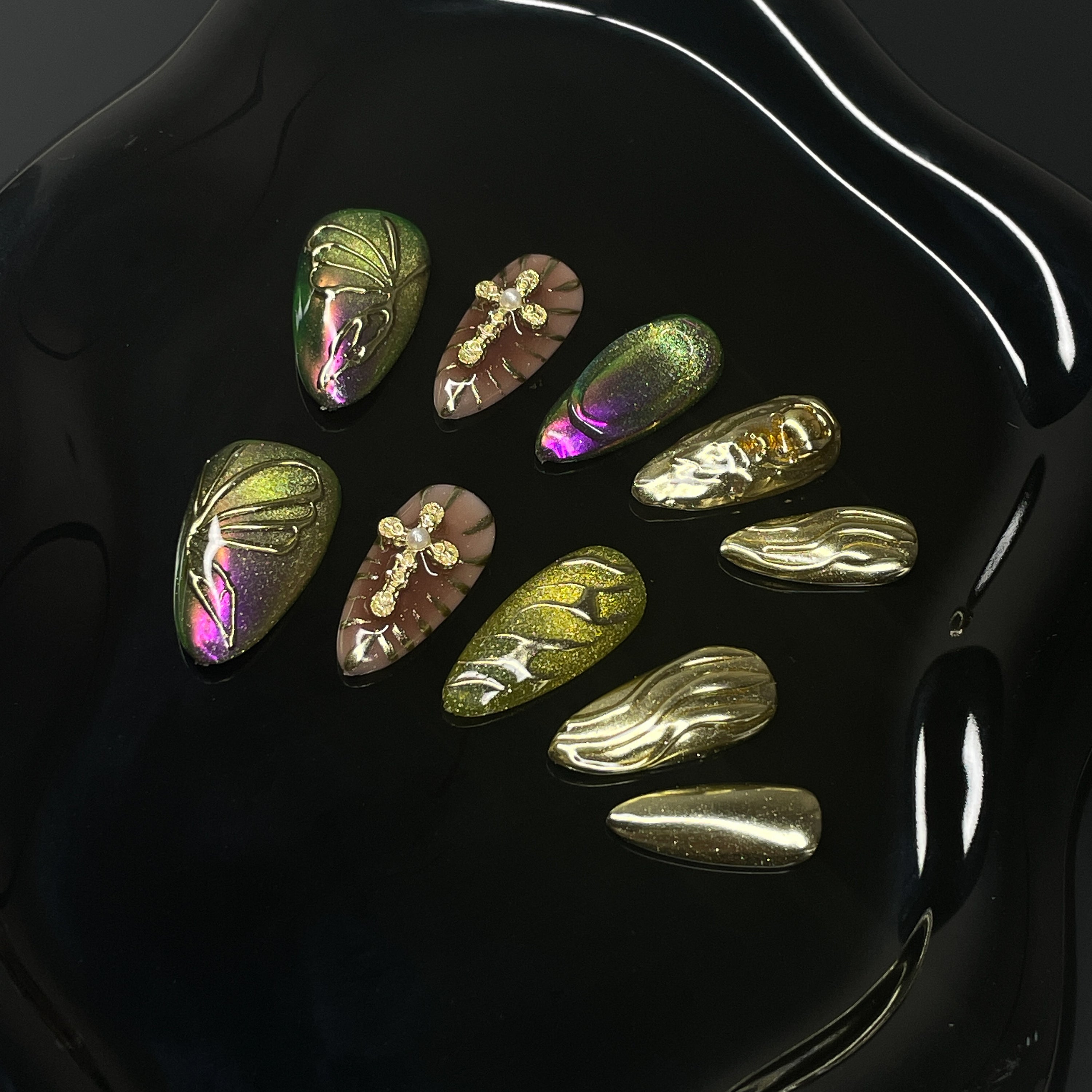 Chameleon Chrome: Green-to-purple shifts that catch light like beetle wings or deep forest reflections.
• 3D Butterfly Wing Details: Raised lines mimic delicate wing structures for an organic, airy look.
• Metallic Gold Accents: Flowing molten textures and glossy gold charms add luxury and warmth.
• Insect-Inspired Embellishments: Golden dragonflies and soft glitter give it a fairy garden feel.
• Almond Shape: A soft and wearable silhouette that perfectly balances bold color with delicate details.