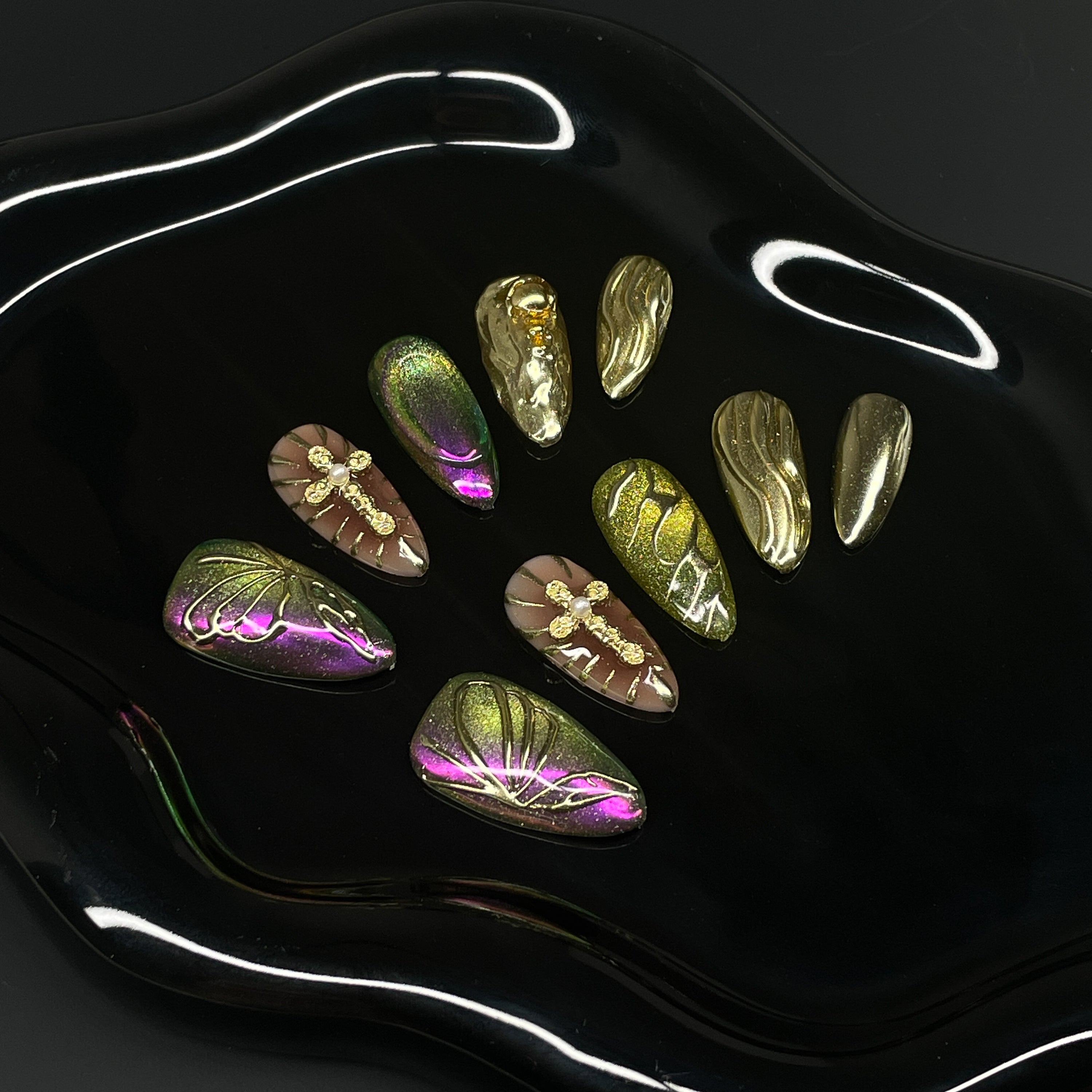 Chameleon Chrome: Green-to-purple shifts that catch light like beetle wings or deep forest reflections.
• 3D Butterfly Wing Details: Raised lines mimic delicate wing structures for an organic, airy look.
• Metallic Gold Accents: Flowing molten textures and glossy gold charms add luxury and warmth.
• Insect-Inspired Embellishments: Golden dragonflies and soft glitter give it a fairy garden feel.
• Almond Shape: A soft and wearable silhouette that perfectly balances bold color with delicate details.