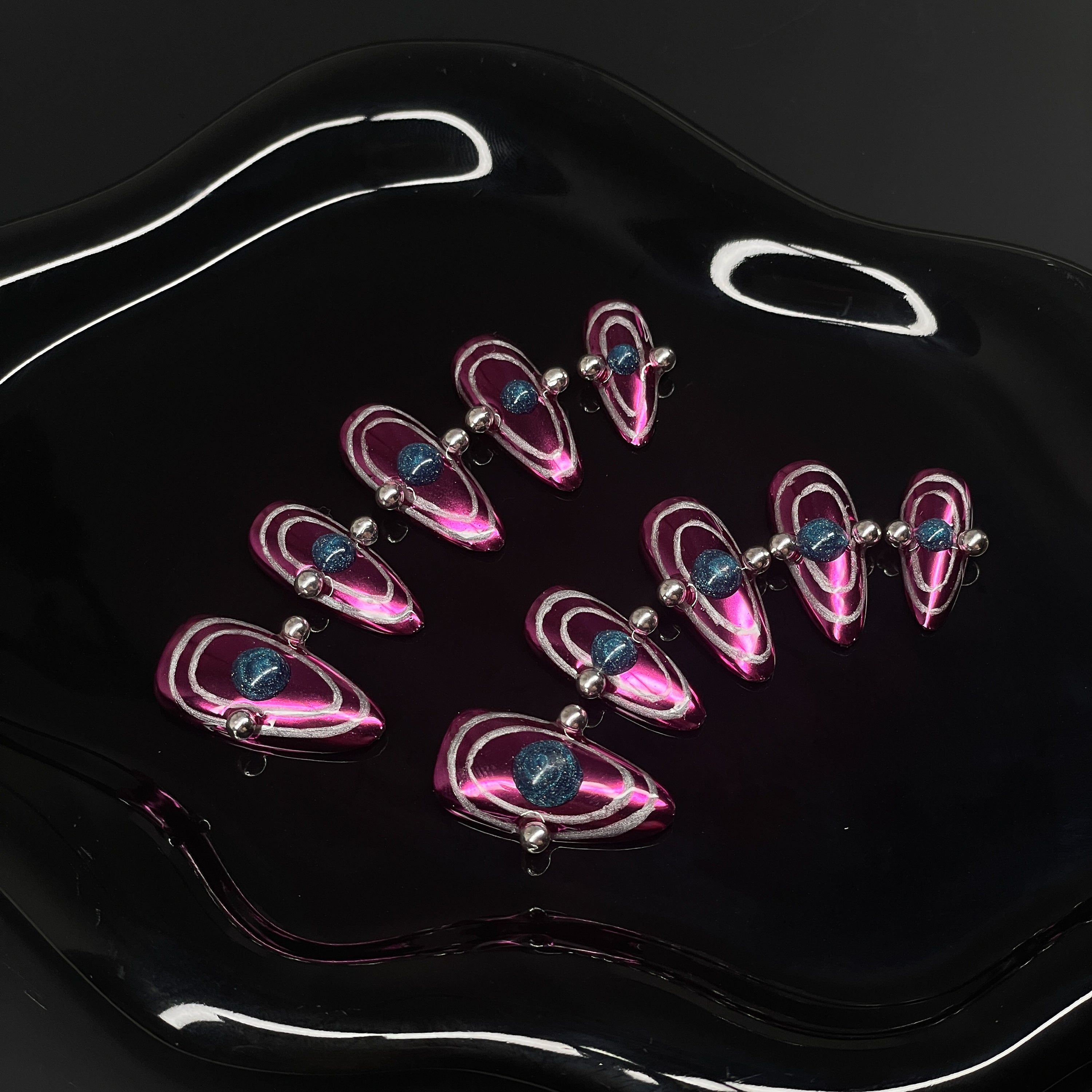Chrome Pink Power: Vibrant metallic fuchsia base that shines like space metal under starlight.
• Orbital Illusion: Layered rings and 3D gel spheres give the look of planetary motion and galactic pull.
• Metallic Silver Beads: Accented with reflective chrome dots for a hyper-modern, kinetic feel.
• Dimensional Energy: Bold shapes and colors create a striking, space-age optical illusion.
• Almond Shape: Sleek, tapered tips keep the interstellar design elegant and wearable.