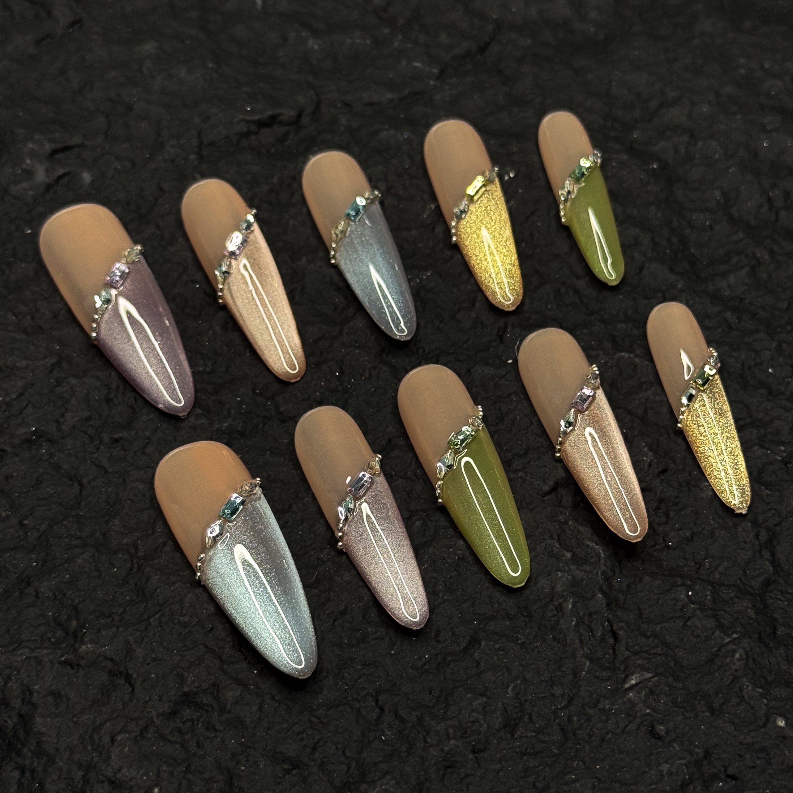 Nude Foundation: Neutral, semi-sheer base tones that flatter every skin tone while keeping things sophisticated.
• Shimmer Gradient: Subtle ombré sparkle in pastel greens, silvers, golds, and blues for a dreamy veil effect.
• Jewel Strap Detail: Diagonal crystal-embellished line wraps the nail like fine jewelry, adding high-end polish.
• Metallic Accents: Tiny gold beads frame the design, balancing shine with softness.
• Long Coffin Shape: Elegant length and squared-off tip ideal for both special events and