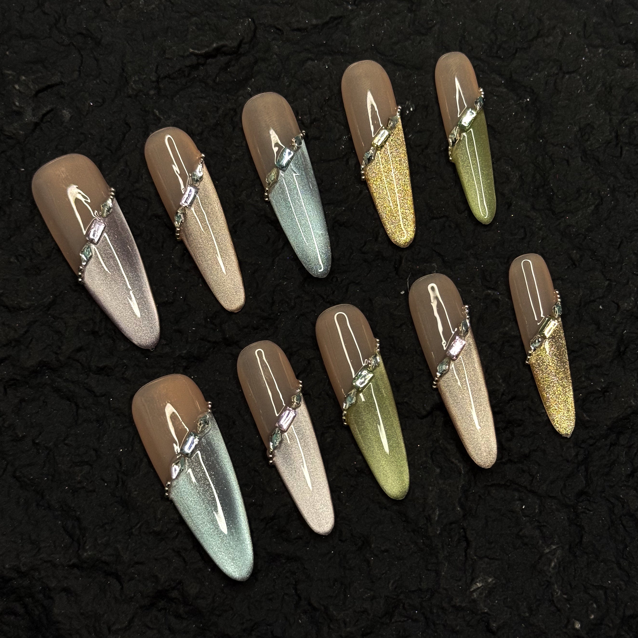 Nude Foundation: Neutral, semi-sheer base tones that flatter every skin tone while keeping things sophisticated.
• Shimmer Gradient: Subtle ombré sparkle in pastel greens, silvers, golds, and blues for a dreamy veil effect.
• Jewel Strap Detail: Diagonal crystal-embellished line wraps the nail like fine jewelry, adding high-end polish.
• Metallic Accents: Tiny gold beads frame the design, balancing shine with softness.
• Long Coffin Shape: Elegant length and squared-off tip ideal for both special events and