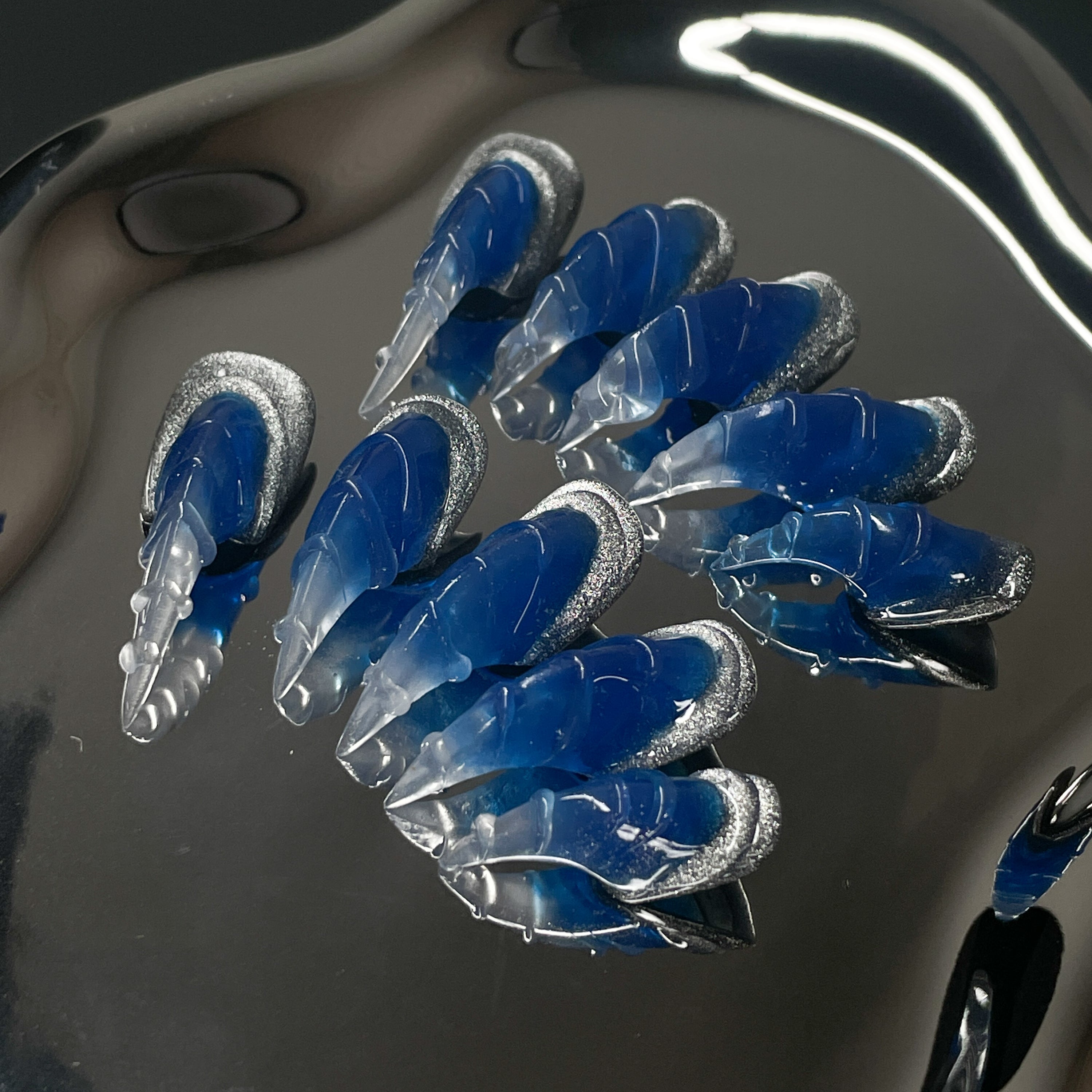 Glacier Blue Ombre: Frosty blues fade into translucent crystal tips like ice breaking over deep water.
• 3D Claw Sculpt: Each nail is shaped with fierce, curved ridges for a wild, talon-like silhouette.
• Silver Ice Accents: Glittery chrome edges mimic frozen crusts and shimmering snow.
• Frosted Finish: A mix of matte and gloss textures gives this set the ultimate arctic edge.
• Claw Shape: Sharp, sculpted tips that extend like icy weapons—bold, edgy, and unapologetic.