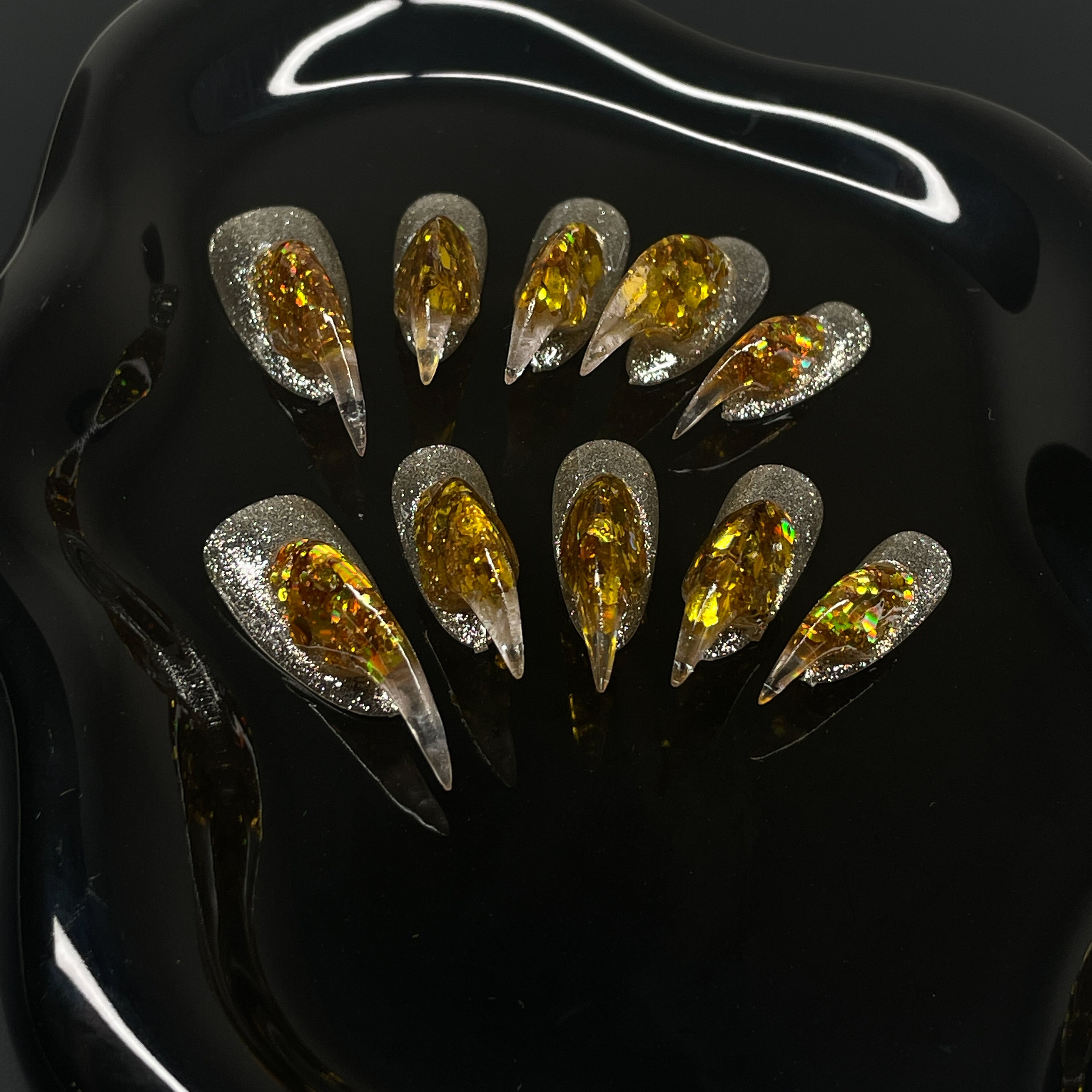  Holographic Gold Core: Encased flake foil burns bright inside a clear, sculpted gel spike.
• Silver Glitter Base: A sparkling foundation adds icy contrast to the molten glow.
• Fierce 3D Sculpting: Each nail rises into a pointed, claw-like peak for maximum visual impact.
• Light-Catching Brilliance: Multidimensional shine that shifts with every move.
• Claw Shape: Aggressively sculpted tips for a fierce, futuristic finish that bites back.