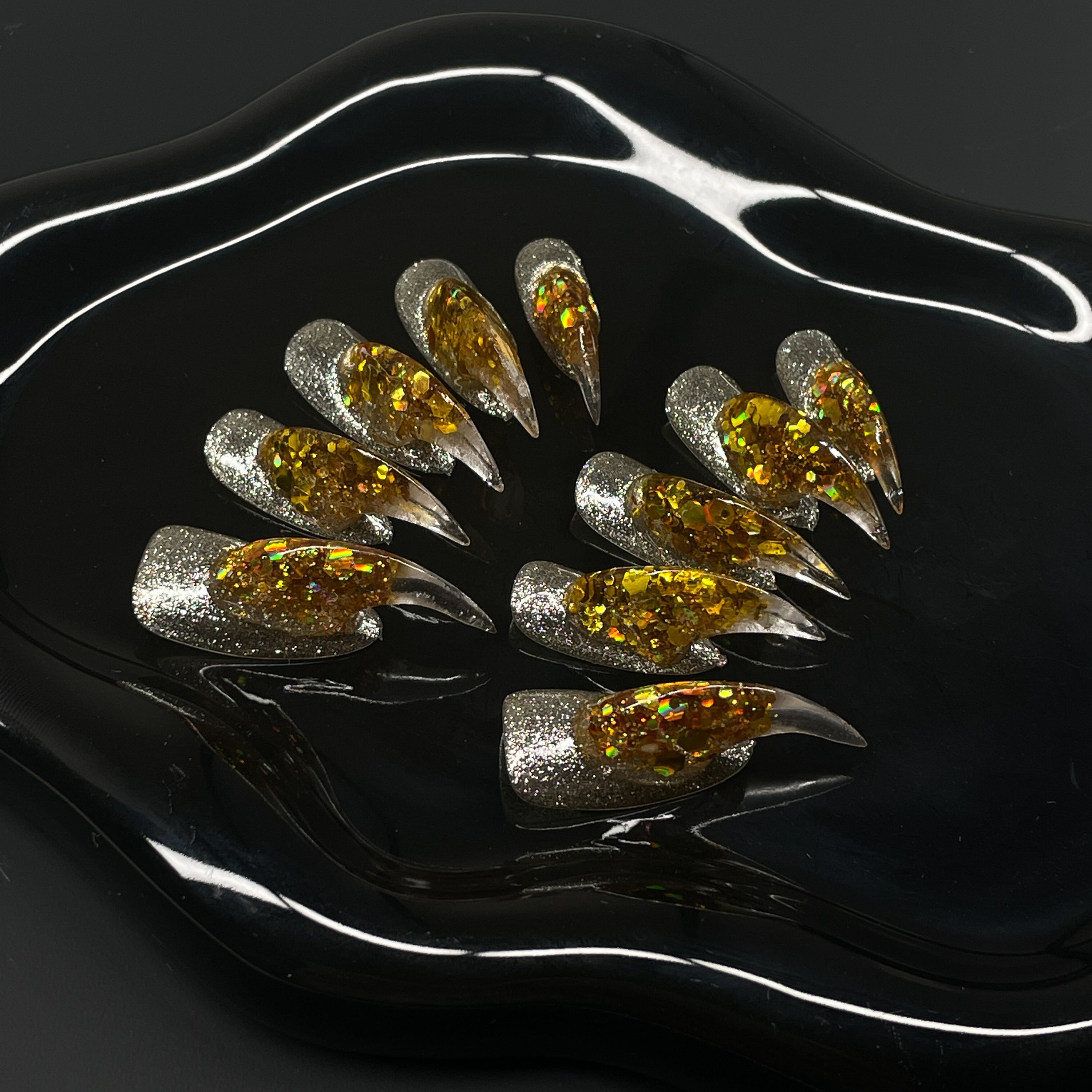  Holographic Gold Core: Encased flake foil burns bright inside a clear, sculpted gel spike.
• Silver Glitter Base: A sparkling foundation adds icy contrast to the molten glow.
• Fierce 3D Sculpting: Each nail rises into a pointed, claw-like peak for maximum visual impact.
• Light-Catching Brilliance: Multidimensional shine that shifts with every move.
• Claw Shape: Aggressively sculpted tips for a fierce, futuristic finish that bites back.