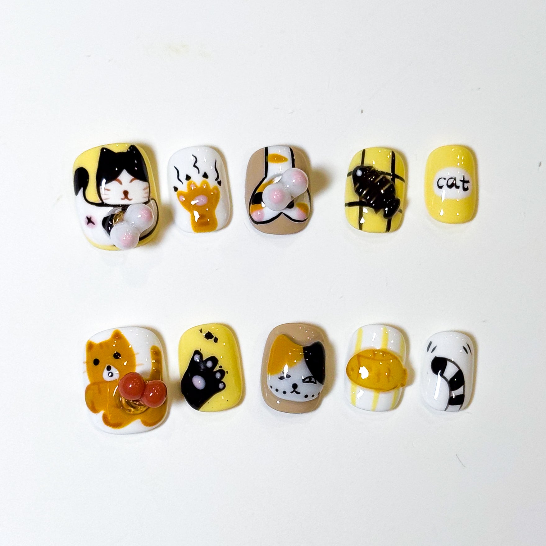 • Adorable Cat Art: Hand-painted kitty faces in orange and calico with the cutest expressions.
• 3D Paw Details: Puffy jellybean paw pads you’ll want to boop all day.
• Playful Motifs: Fish bones, yarn balls, and the word “cat” in bold black for extra whimsy.
• Cheerful Colors: A happy palette of yellow, orange, white, and black.
• Short Square Shape: Easy to wear daily while keeping the design bold and fun.
