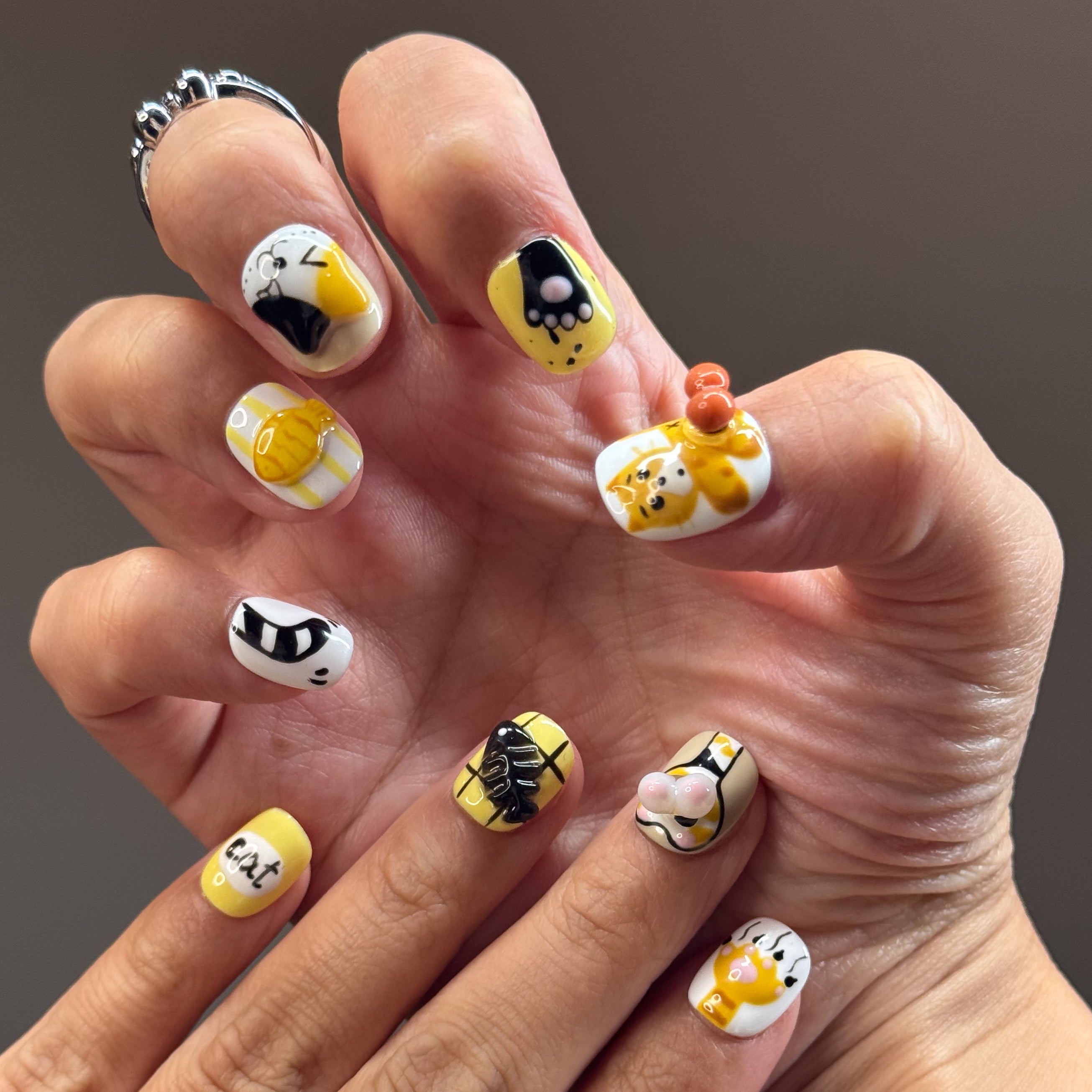 • Adorable Cat Art: Hand-painted kitty faces in orange and calico with the cutest expressions.
• 3D Paw Details: Puffy jellybean paw pads you’ll want to boop all day.
• Playful Motifs: Fish bones, yarn balls, and the word “cat” in bold black for extra whimsy.
• Cheerful Colors: A happy palette of yellow, orange, white, and black.
• Short Square Shape: Easy to wear daily while keeping the design bold and fun.