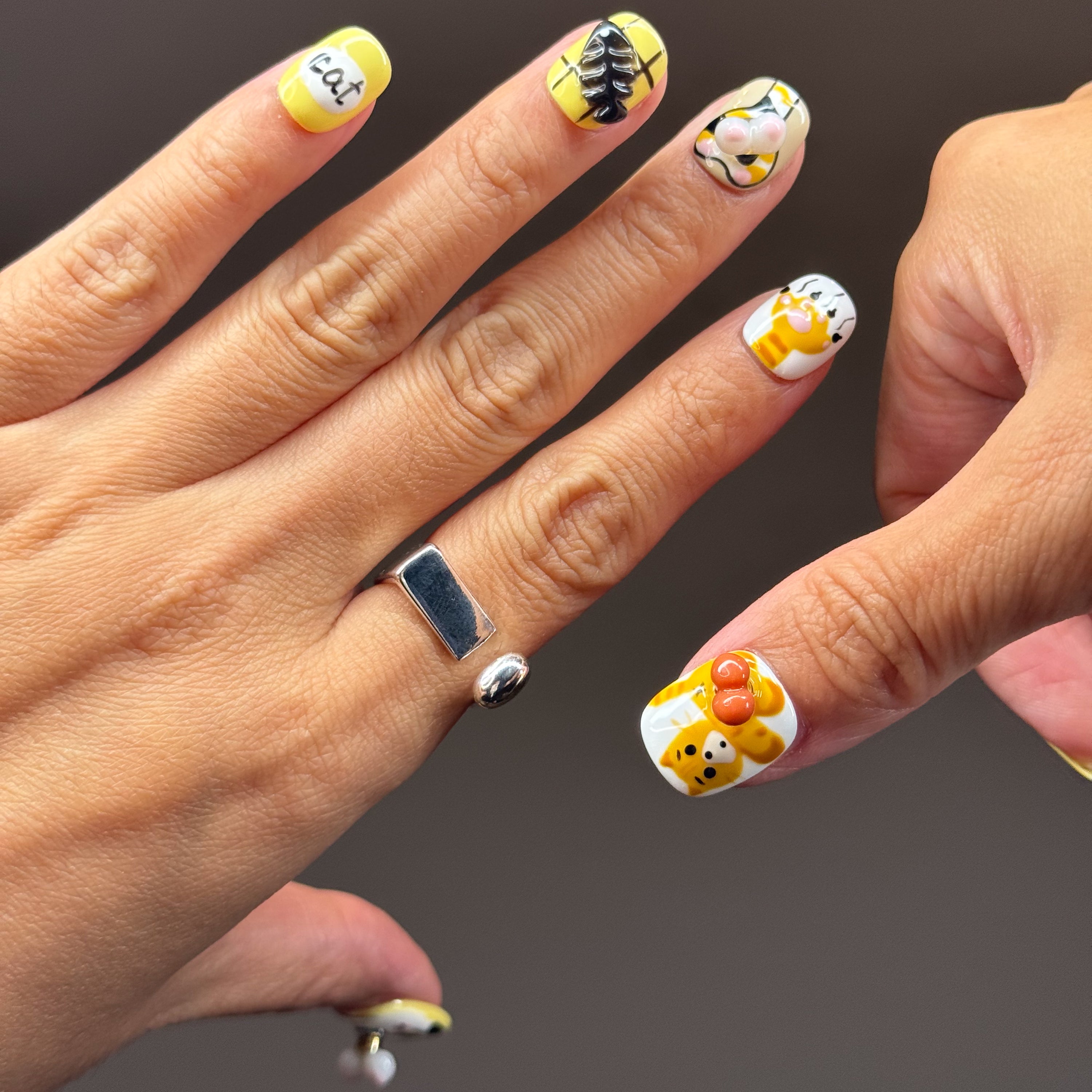 • Adorable Cat Art: Hand-painted kitty faces in orange and calico with the cutest expressions.
• 3D Paw Details: Puffy jellybean paw pads you’ll want to boop all day.
• Playful Motifs: Fish bones, yarn balls, and the word “cat” in bold black for extra whimsy.
• Cheerful Colors: A happy palette of yellow, orange, white, and black.
• Short Square Shape: Easy to wear daily while keeping the design bold and fun.