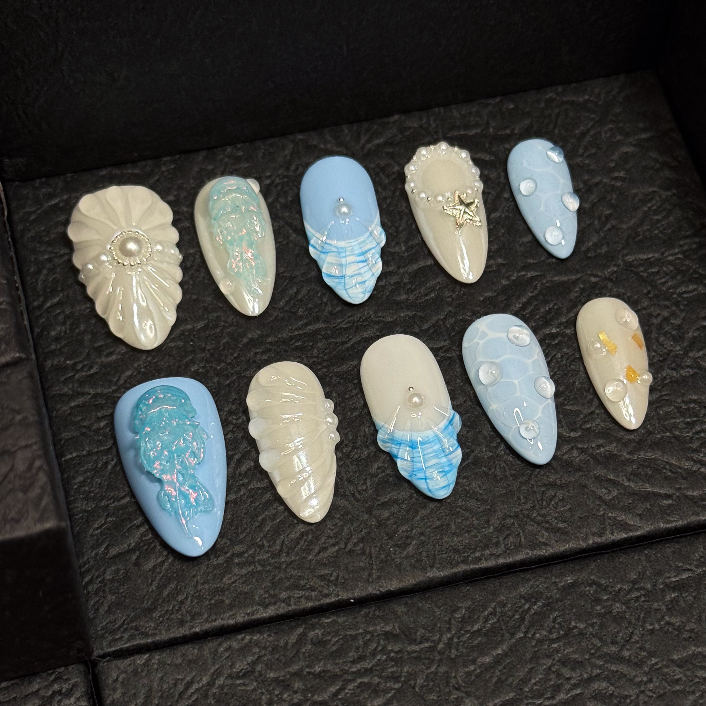 Coastal Color Story: Cool pastel blues and creamy pearls bring breezy, beachy elegance.
• Sculpted Sea Motifs: 3D jellyfish, starfish, and shell ridges turn each nail into a tiny seascape.
• Iridescent Glow: Opal shimmer and pearl accents mimic the glisten of sea foam and sunlight on water.
• Unique Ocean Textures: Bubble effects, netting patterns, and wave-like lines evoke the depth of the deep sea.
• Almond Shape: Sleek and feminine, perfect for balancing oceanic whimsy with everyday wear.