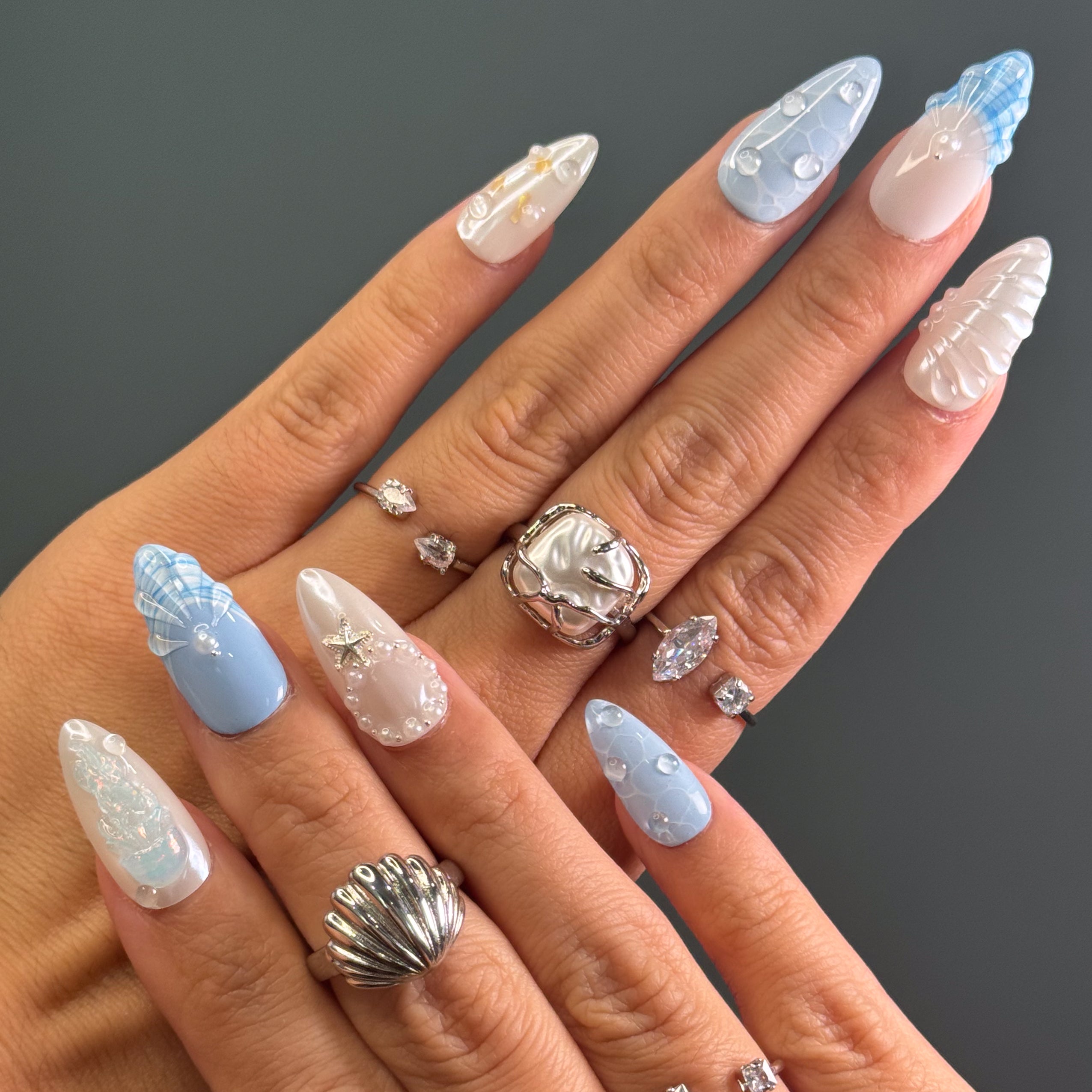 Coastal Color Story: Cool pastel blues and creamy pearls bring breezy, beachy elegance.
• Sculpted Sea Motifs: 3D jellyfish, starfish, and shell ridges turn each nail into a tiny seascape.
• Iridescent Glow: Opal shimmer and pearl accents mimic the glisten of sea foam and sunlight on water.
• Unique Ocean Textures: Bubble effects, netting patterns, and wave-like lines evoke the depth of the deep sea.
• Almond Shape: Sleek and feminine, perfect for balancing oceanic whimsy with everyday wear.