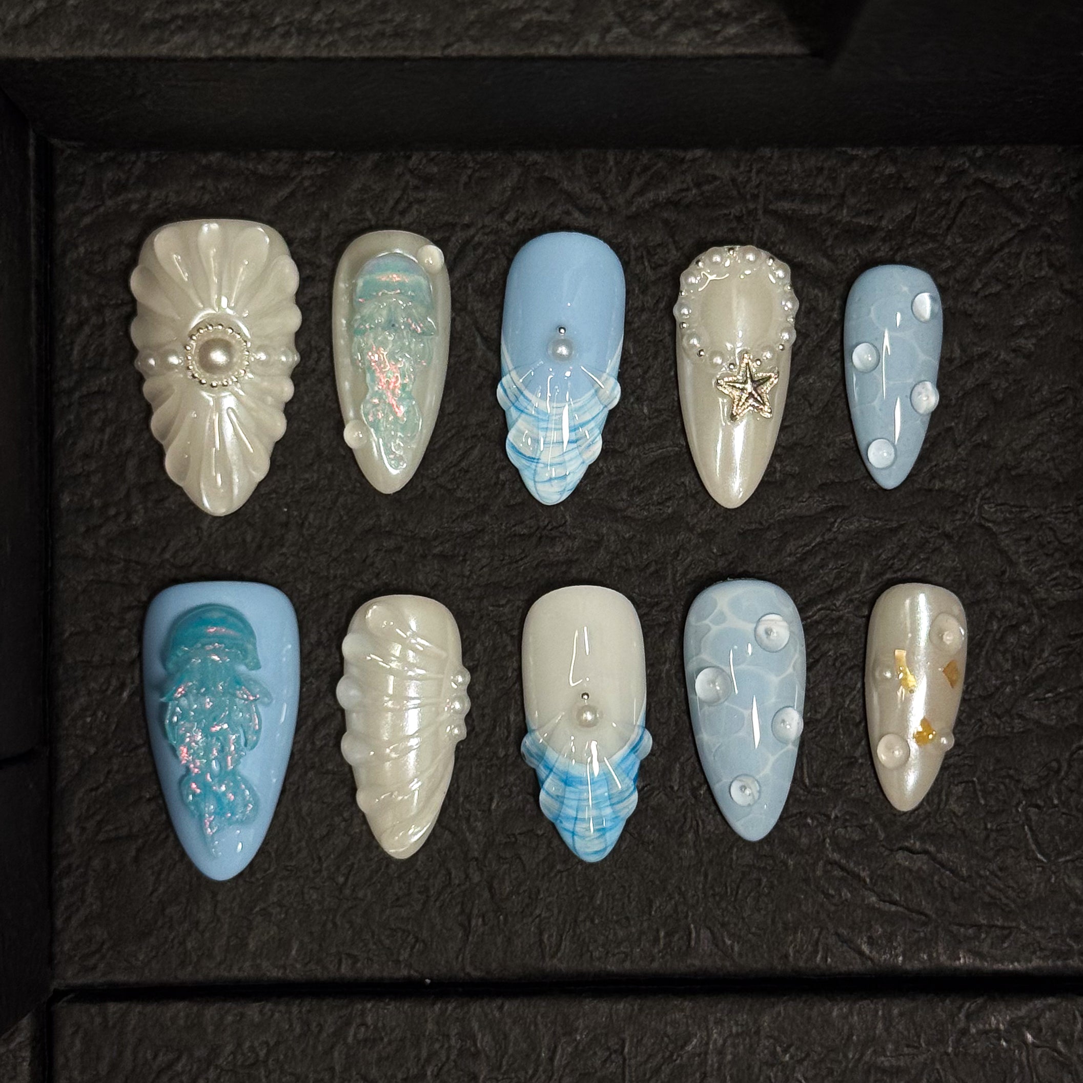 Coastal Color Story: Cool pastel blues and creamy pearls bring breezy, beachy elegance.
• Sculpted Sea Motifs: 3D jellyfish, starfish, and shell ridges turn each nail into a tiny seascape.
• Iridescent Glow: Opal shimmer and pearl accents mimic the glisten of sea foam and sunlight on water.
• Unique Ocean Textures: Bubble effects, netting patterns, and wave-like lines evoke the depth of the deep sea.
• Almond Shape: Sleek and feminine, perfect for balancing oceanic whimsy with everyday wear.