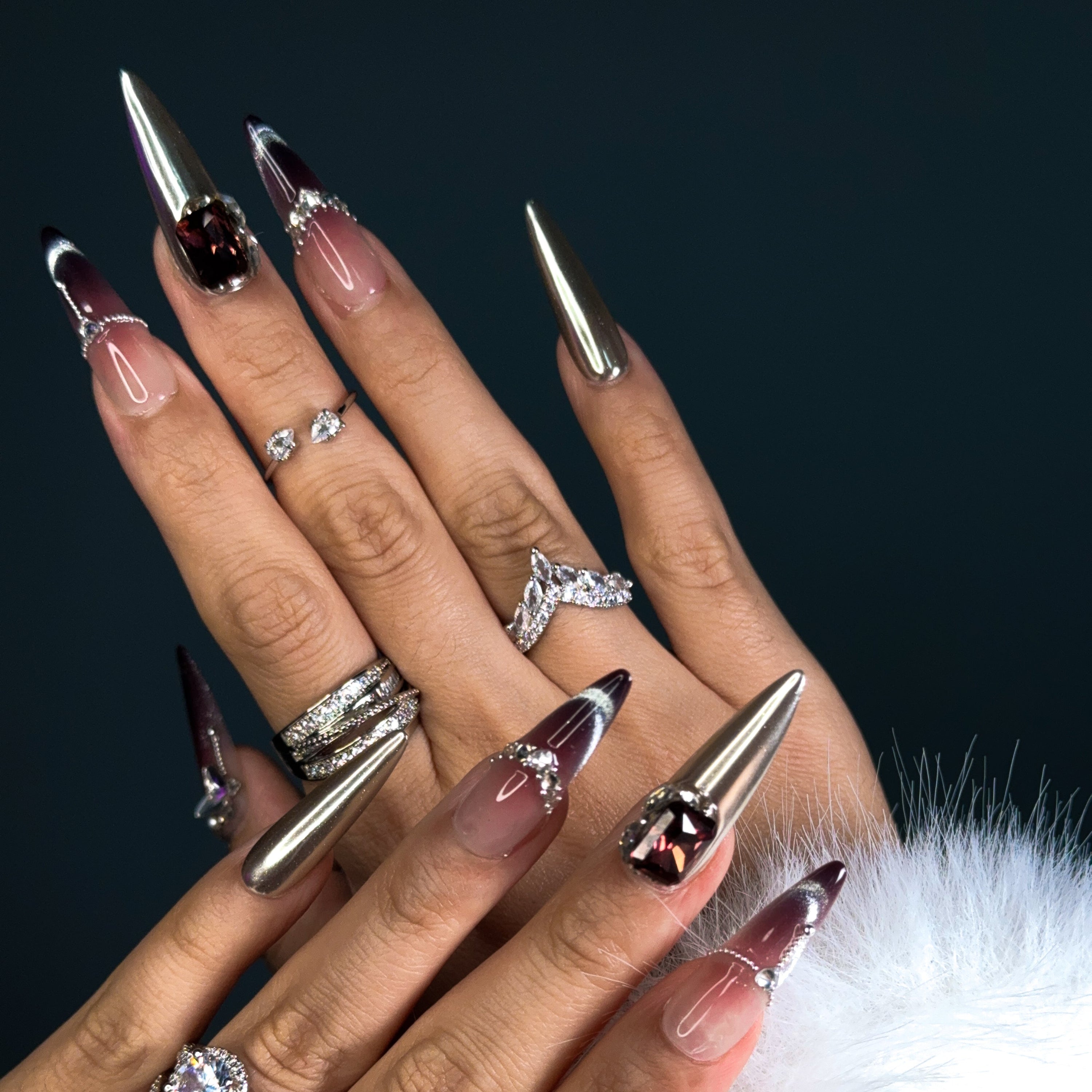 Indulge in pure luxury with Royal Mirage Press-On Nails. These extra-long stiletto nails feature a breathtaking purple ombre blended with silver, creating a regal and enchanting look. Accented with dazzling diamonds and gemstone decorations, each nail sparkles with elegance. A mirror-like full silver nail adds a bold, high-fashion edge, while the cat-eye effect enhances the depth and mystery of the design.
