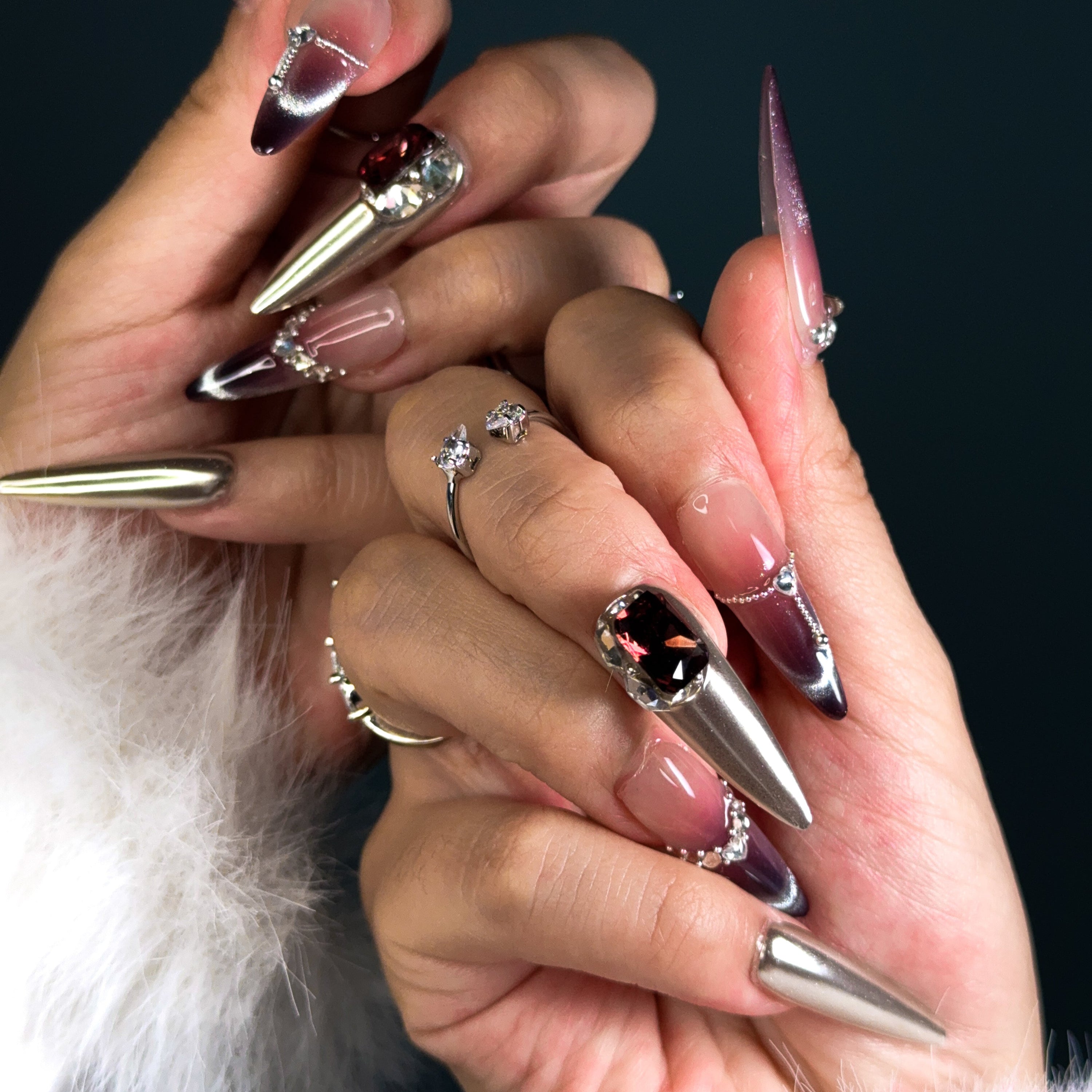 Indulge in pure luxury with Royal Mirage Press-On Nails. These extra-long stiletto nails feature a breathtaking purple ombre blended with silver, creating a regal and enchanting look. Accented with dazzling diamonds and gemstone decorations, each nail sparkles with elegance. A mirror-like full silver nail adds a bold, high-fashion edge, while the cat-eye effect enhances the depth and mystery of the design.
