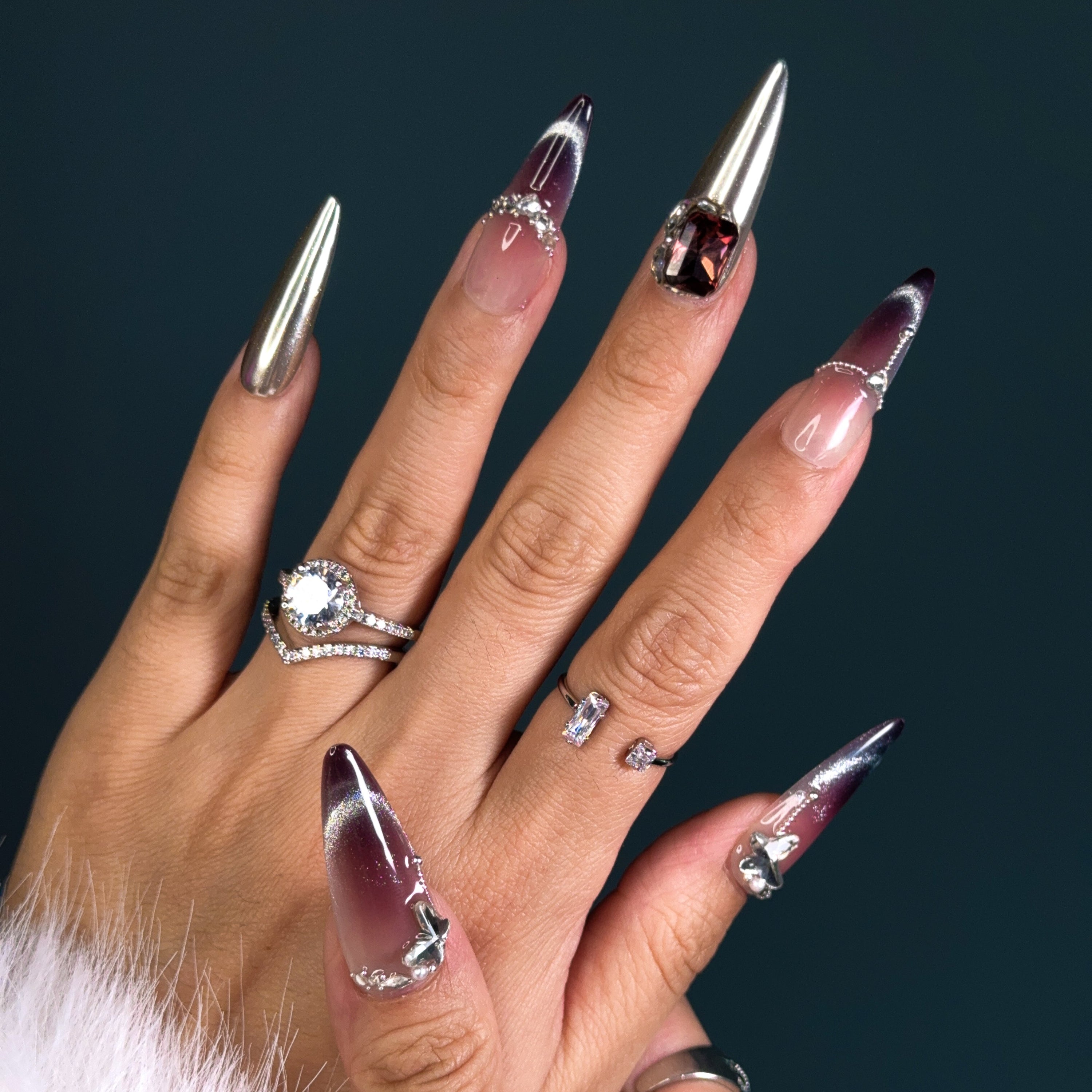Indulge in pure luxury with Royal Mirage Press-On Nails. These extra-long stiletto nails feature a breathtaking purple ombre blended with silver, creating a regal and enchanting look. Accented with dazzling diamonds and gemstone decorations, each nail sparkles with elegance. A mirror-like full silver nail adds a bold, high-fashion edge, while the cat-eye effect enhances the depth and mystery of the design.