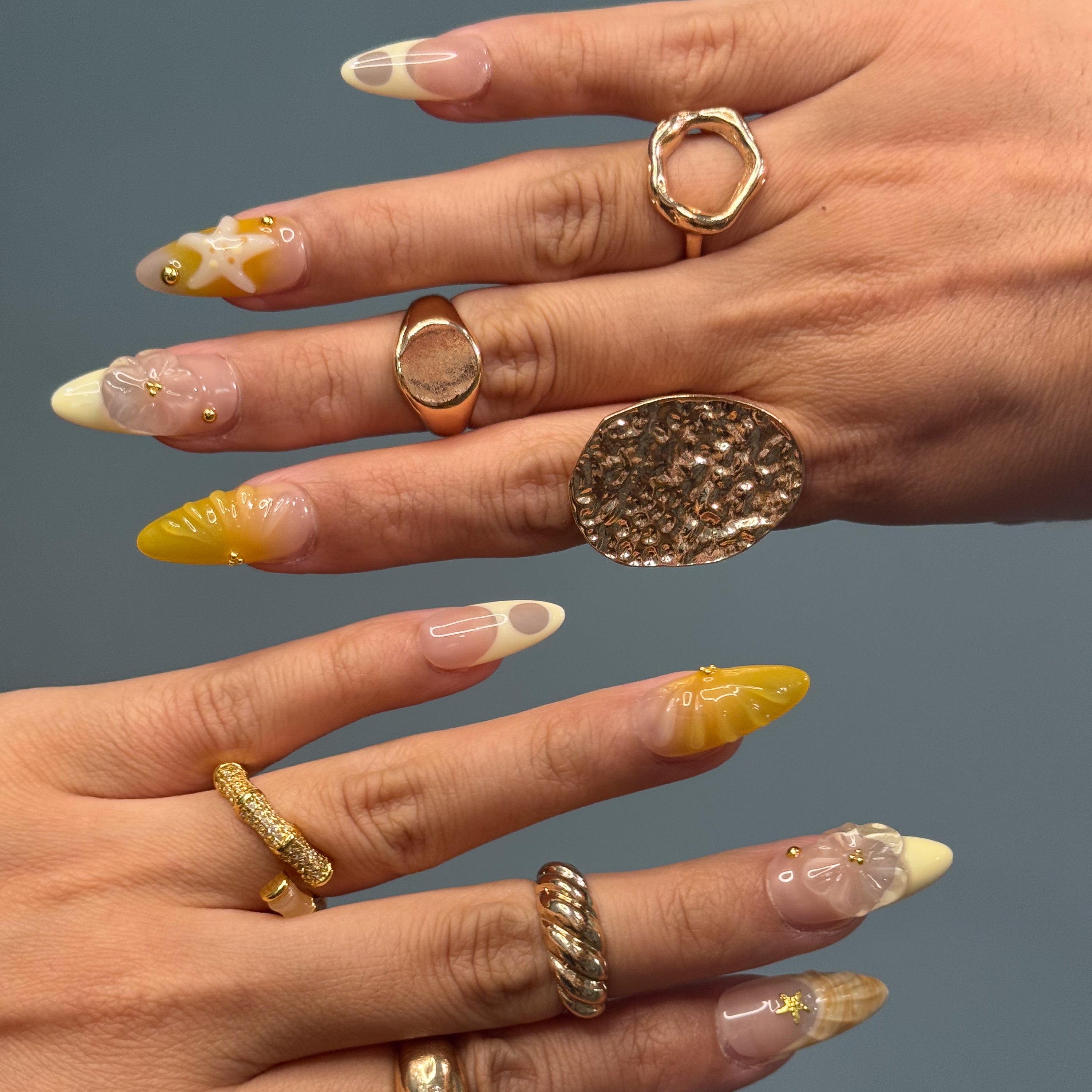 Coastal Color Palette: Taupe, honey yellow, ivory cream, and shell-inspired swirls for that sun-bleached vibe.
• 3D Starfish & Flowers: Hand-sculpted ocean motifs bring depth and summer romance to each nail.
• Textured Shell Accents: Wave-like and seashell textures evoke the feeling of walking barefoot on warm sand.
• Gold Bead Embellishments: Delicate studs and tiny stars add a glimmer of ocean treasure.
• Almond Shape: Natural, beachy elegance with a soft tapered point perfect for sunny adventures.
