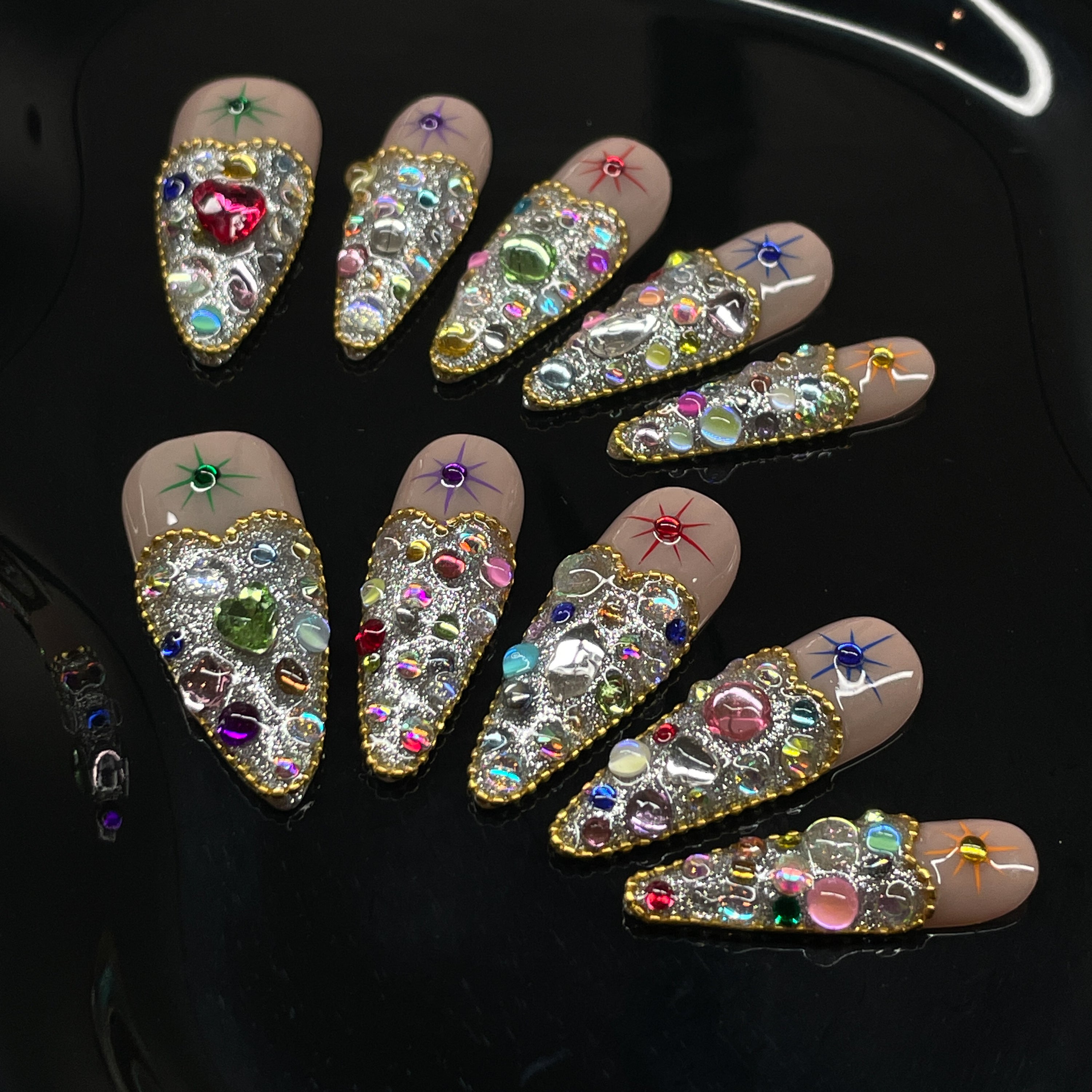 Full Gem Explosion: Packed with multicolored rhinestones, glass crystals, and faceted jewels for instant glam.
• Golden Glitter Base: A bold, sparkling foundation gives each nail the weight of a red carpet moment.
• Starburst Charms: Embedded celestial motifs add a magical pop to every fingertip.
• Luxe Color Palette: Emerald, sapphire, ruby, and amethyst tones blend for a jewel box effect.
• Short Tapered Shape: Compact yet eye-catching—perfect for glam lovers who want comfort and drama.