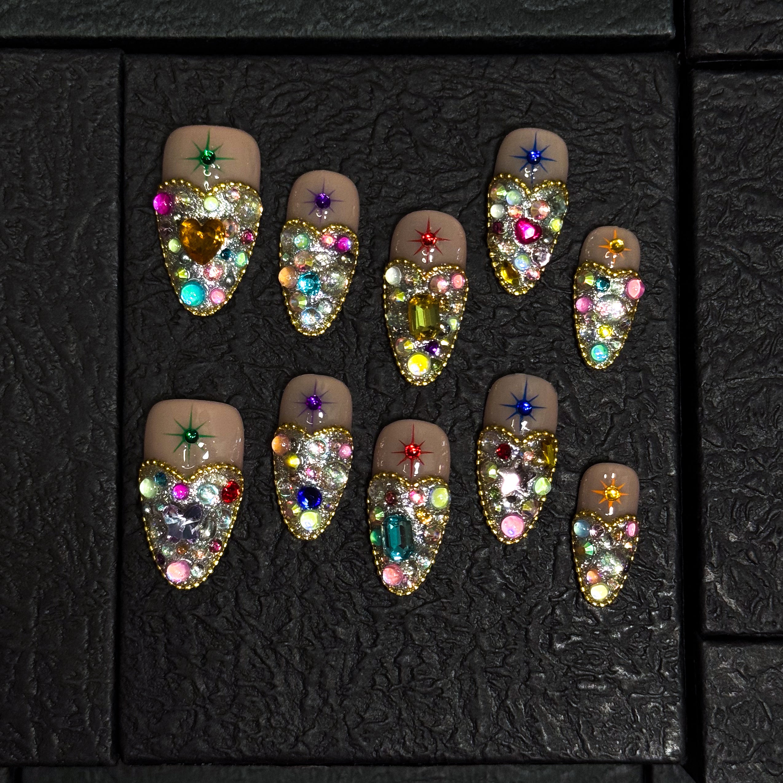 Full Gem Explosion: Packed with multicolored rhinestones, glass crystals, and faceted jewels for instant glam.
• Golden Glitter Base: A bold, sparkling foundation gives each nail the weight of a red carpet moment.
• Starburst Charms: Embedded celestial motifs add a magical pop to every fingertip.
• Luxe Color Palette: Emerald, sapphire, ruby, and amethyst tones blend for a jewel box effect.
• Short Tapered Shape: Compact yet eye-catching—perfect for glam lovers who want comfort and drama.