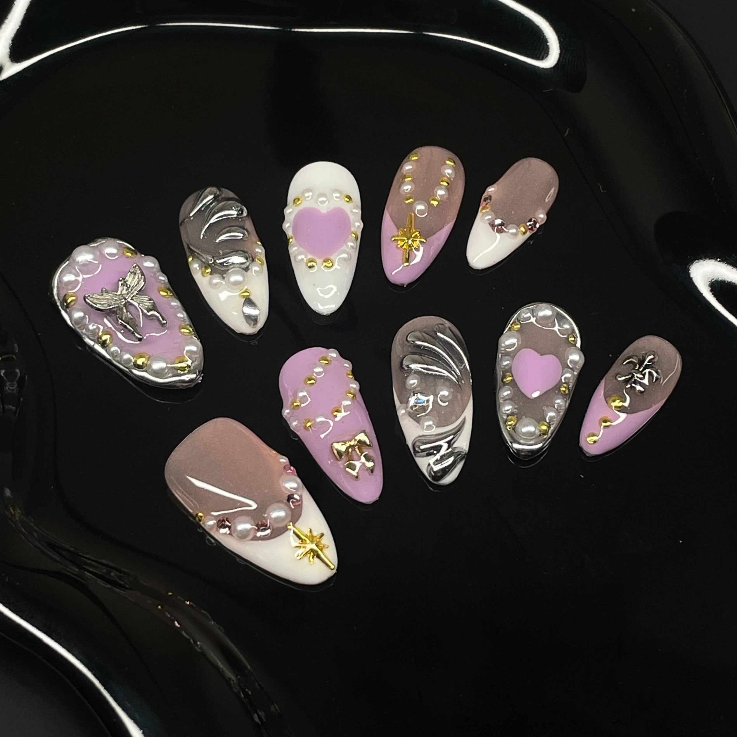 Soft Romantic Tones: A dreamy palette of dusty pink, cocoa brown, ivory, and lavender.
• 3D Heart & Chain Details: Sculpted hearts, pearls, and golden charms give a love-me-but-don’t-cross-me energy.
• Chrome Highlights: Shiny silver and gold accents add edge to the softness.
• Mixed Motifs: Features butterflies, barbed wire, and celestial symbols—where dreamy meets dangerous.
• Almond Shape: Flattering and elegant, this shape balances delicate charm with fierce style.